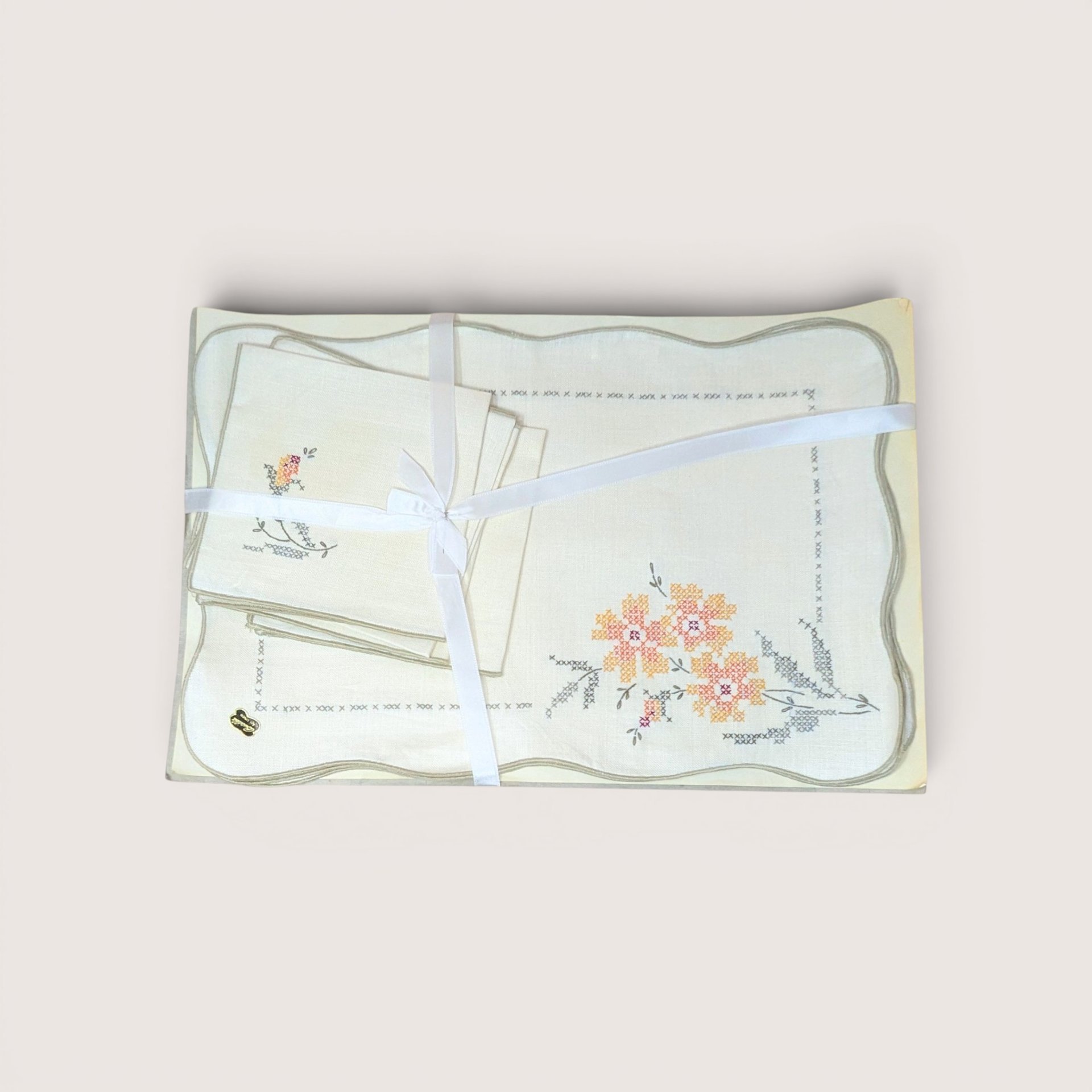 Embroidered linens set with cross-stitch floral designs tied together with a white ribbon, centered on a plain linen background.