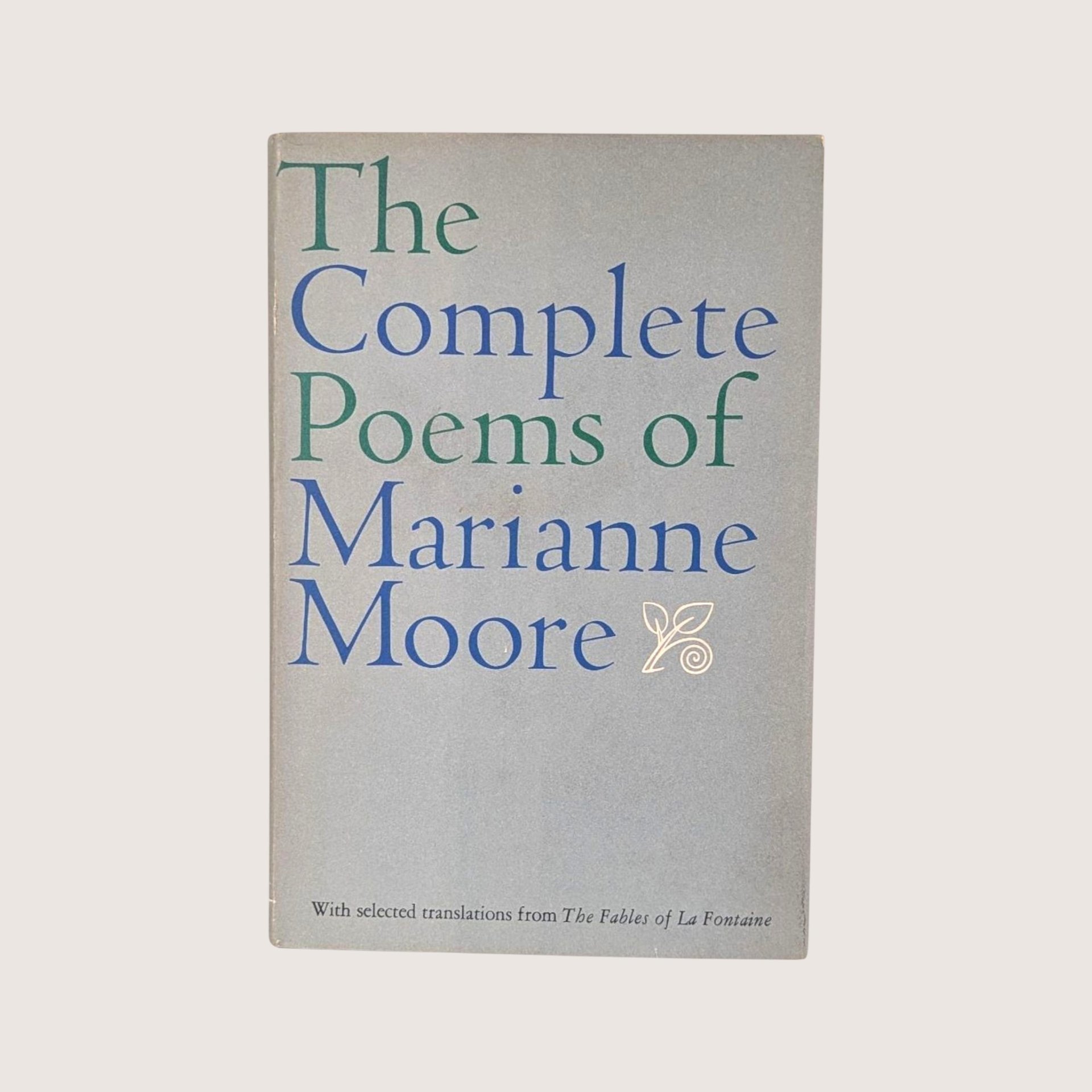 A vintage 1967 hardcover edition of The Complete Poems of Marianne Moore with blue and green typography on a gray dust jacket.