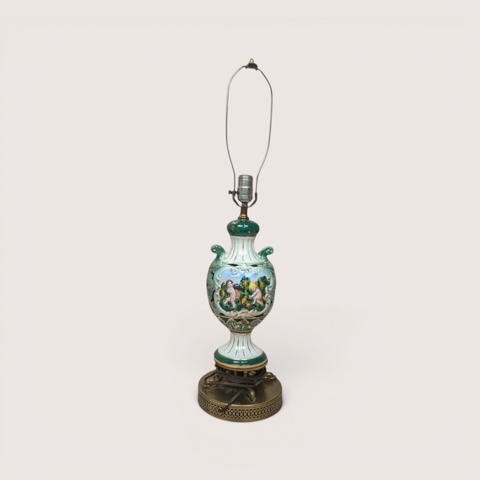 A vintage Italian ceramic table lamp featuring a green and white ornate urn body painted with cherubs.