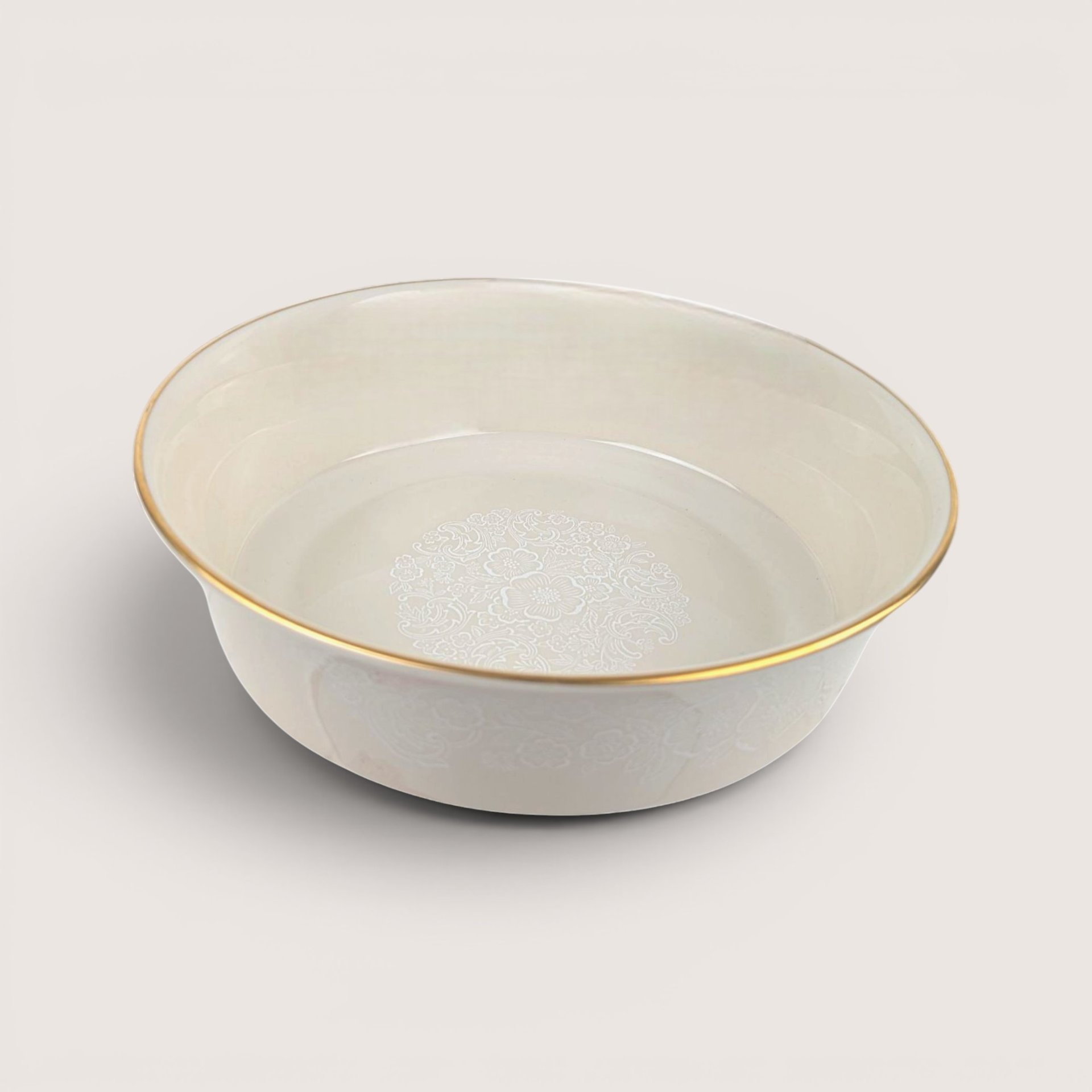 Round ceramic serving bowl with a white floral medallion design on the interior and a gold rim, centered on a plain linen background.