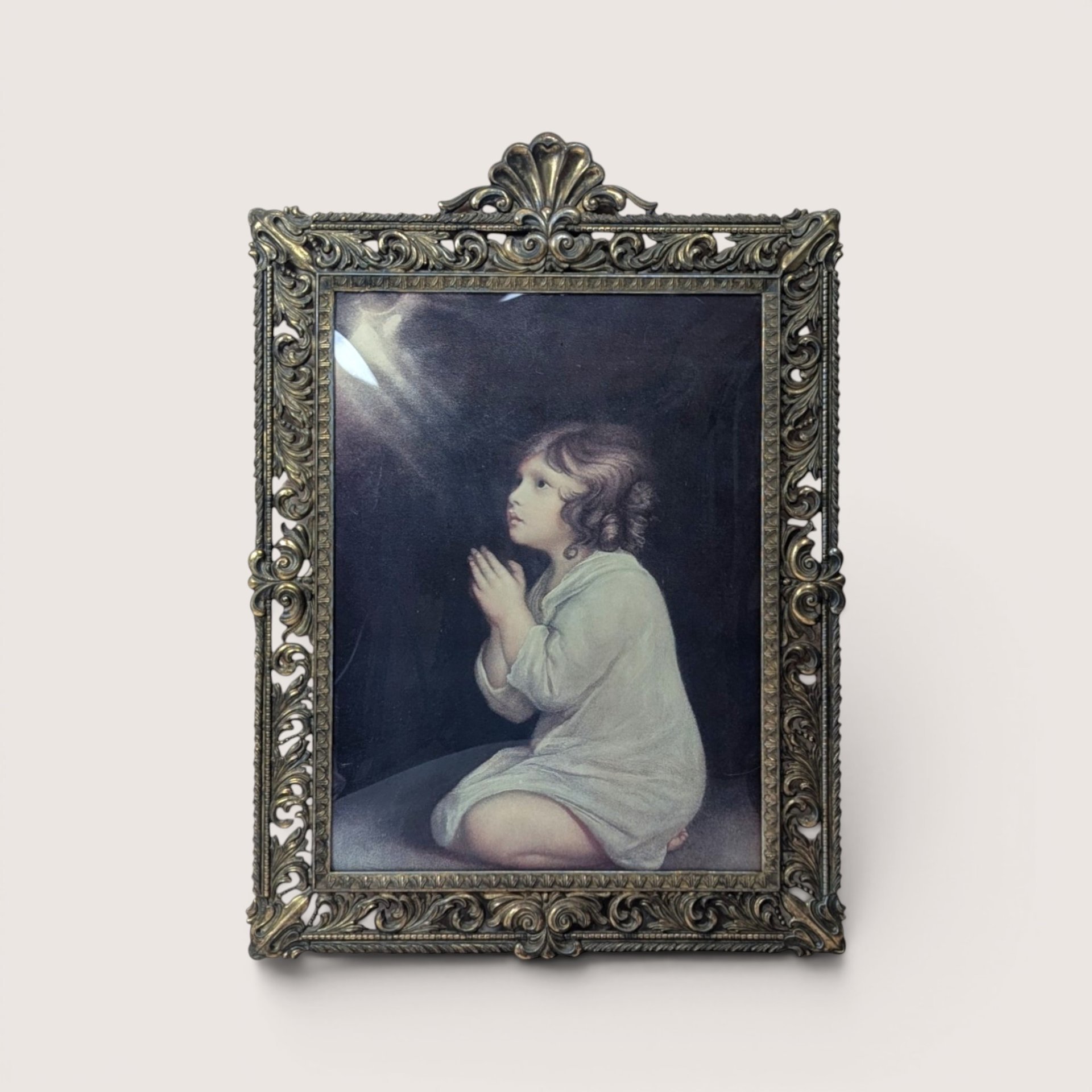 A vintage heavy ornate brass frame holding Sir Joshua Reynolds painting of The Infant Samuel behind curved bubble glass.
