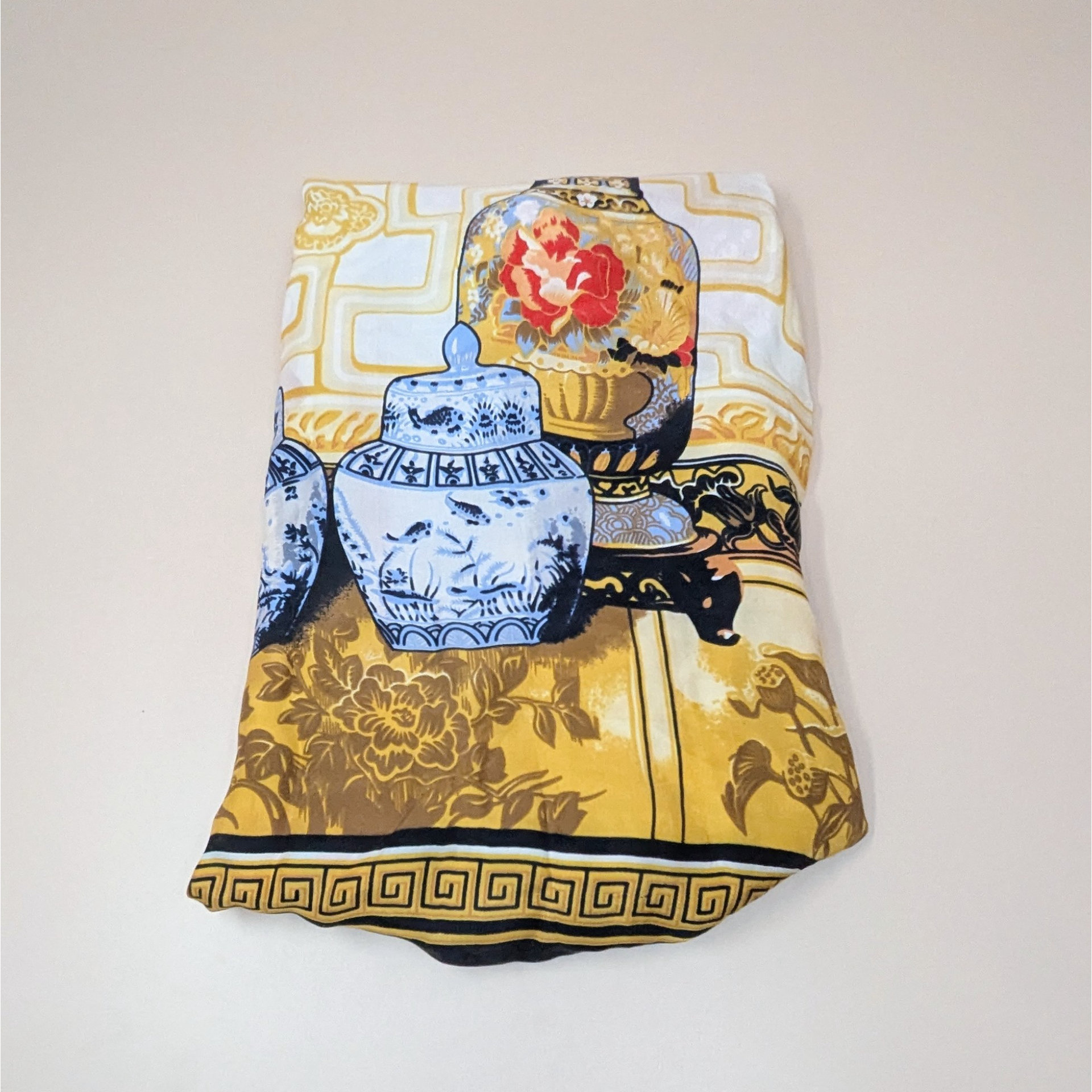 A vintage silk scarf by Huali featuring a print of blue and white ginger jars and floral vases against a warm mustard yellow background. The scarf has a bold black and gold Greek key-style border.