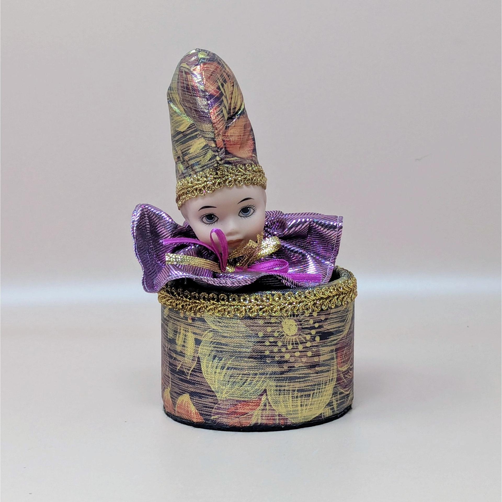 A vintage music box by The San Francisco Music Box Company featuring a porcelain clown head emerging from a floral-patterned base. The clown wears a matching tall hat and a metallic purple ruffled collar.