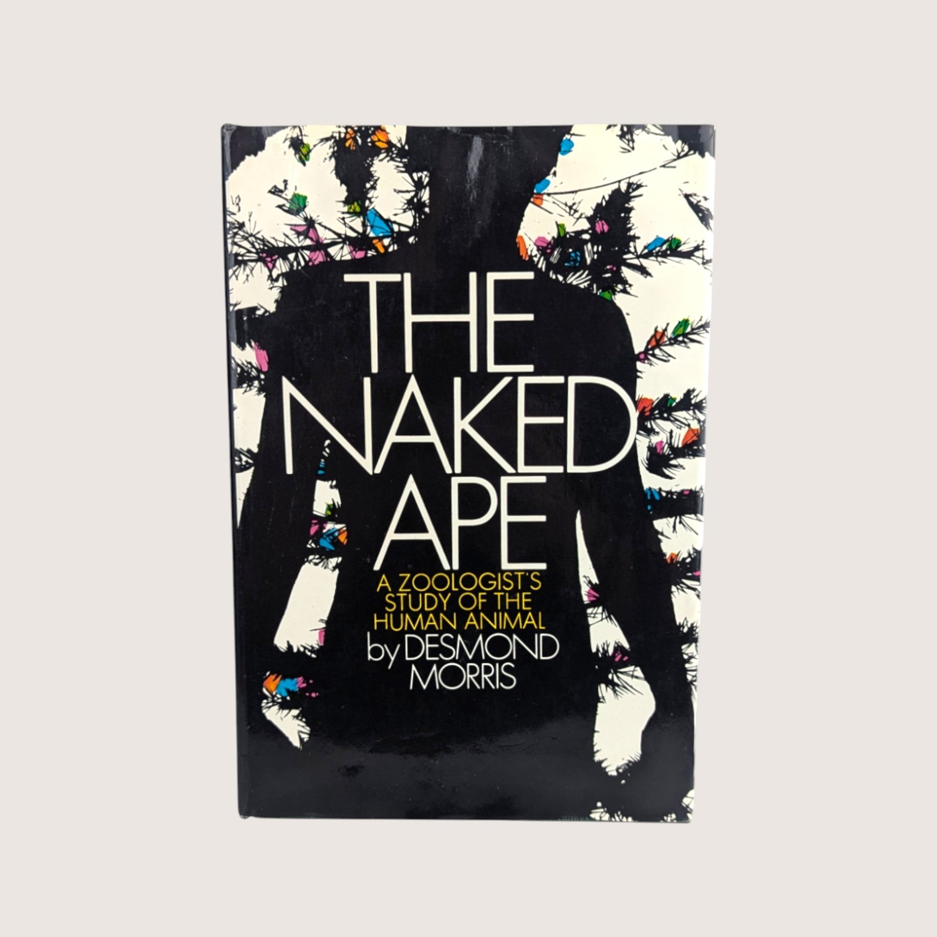 The dust jacket cover of The Naked Ape hardcover book by Desmond Morris featuring a black silhouette with colorful abstract accents.