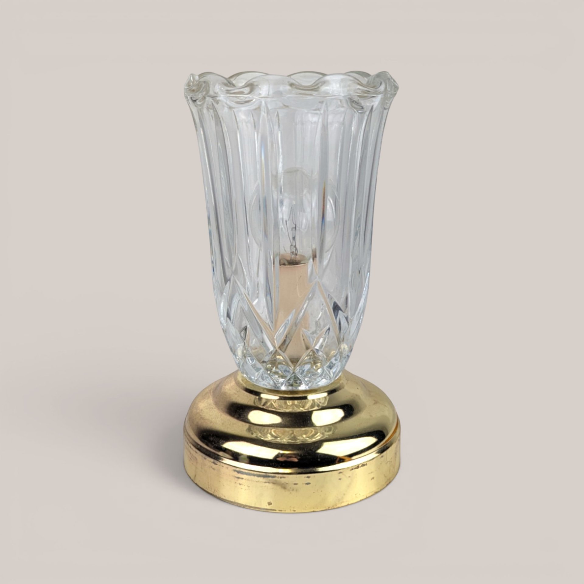 Clear glass tulip chimney lamp with a brass base on a plain background.