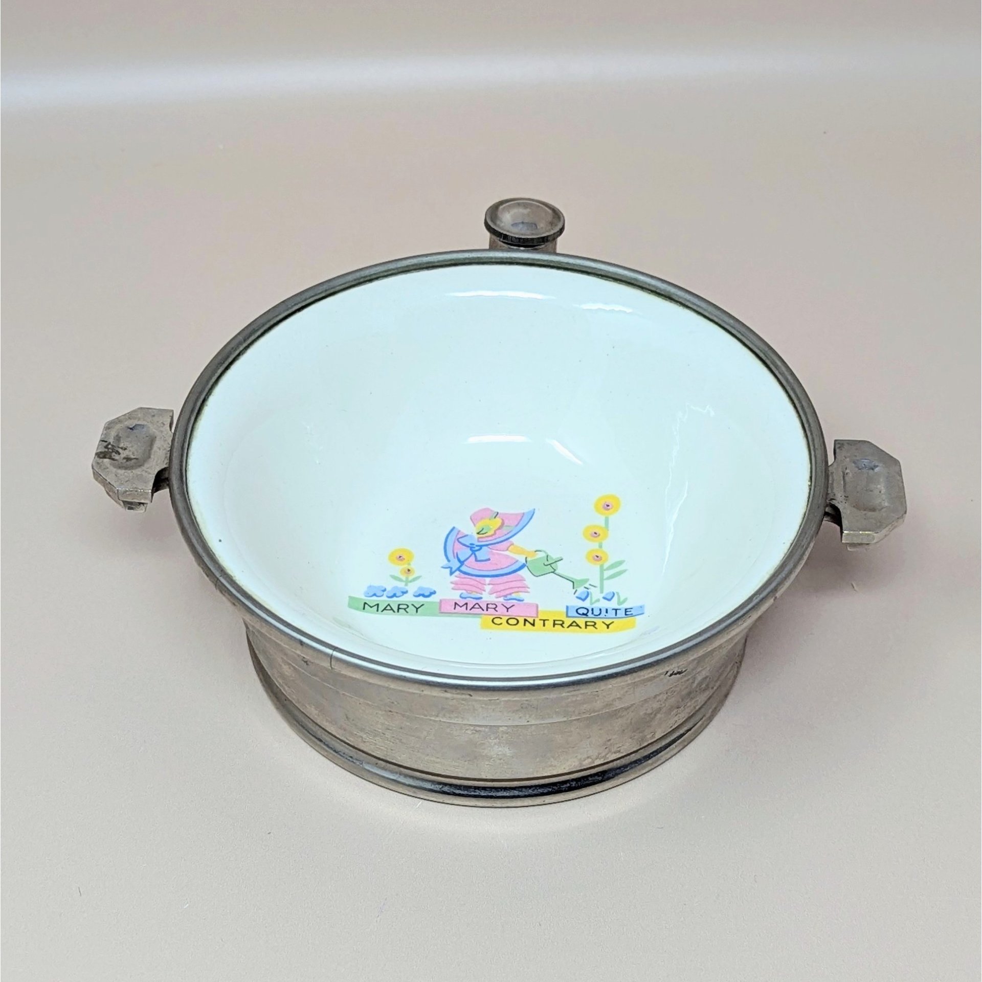 A vintage children's bowl by GW Company featuring an enamel interior with a "Mary Mary Quite Contrary" graphic in the center, set within a polished chrome base with two handles.