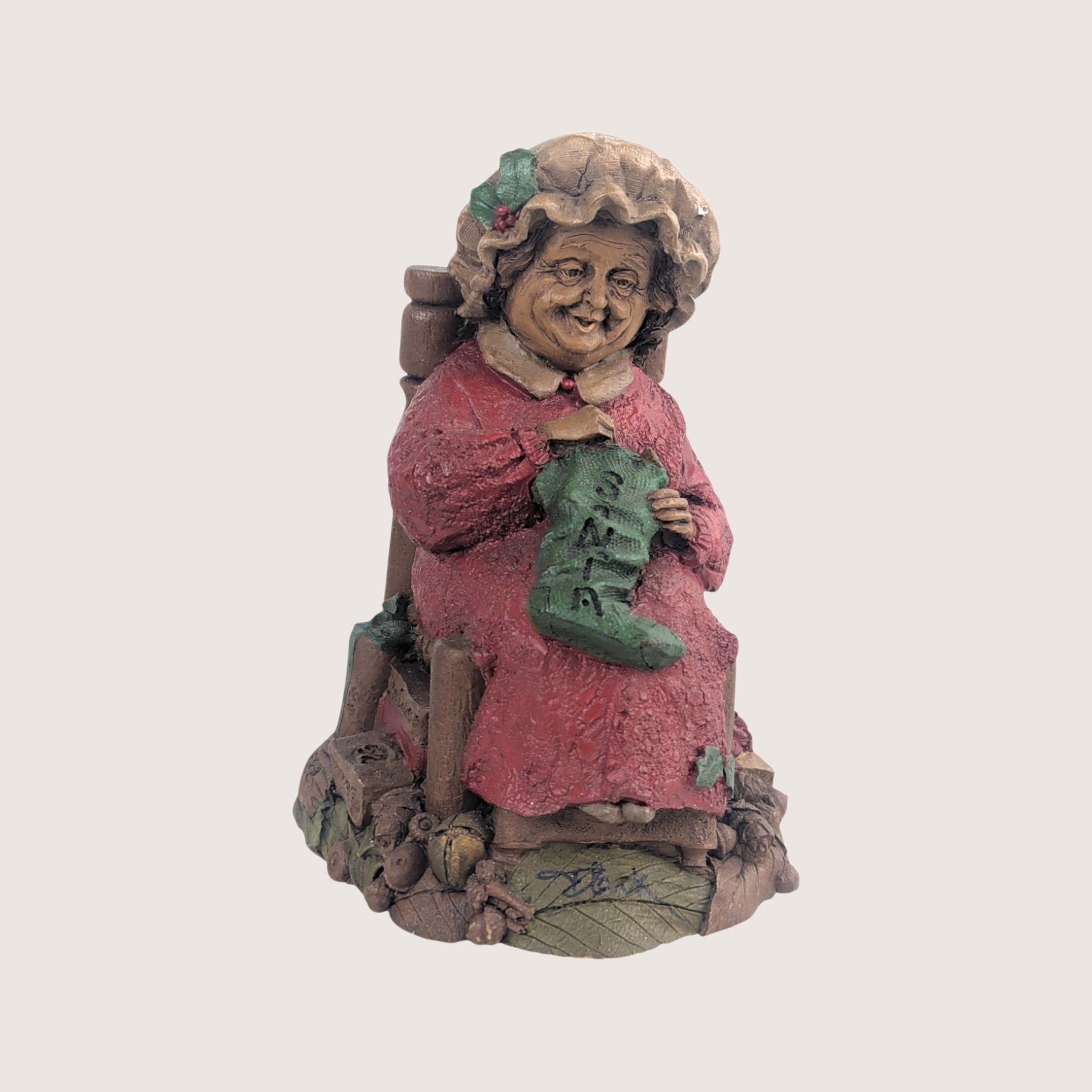 A vintage Tom Clark Cairn Studios resin figurine titled Mrs Claus featuring a woman sitting in a chair knitting a stocking.