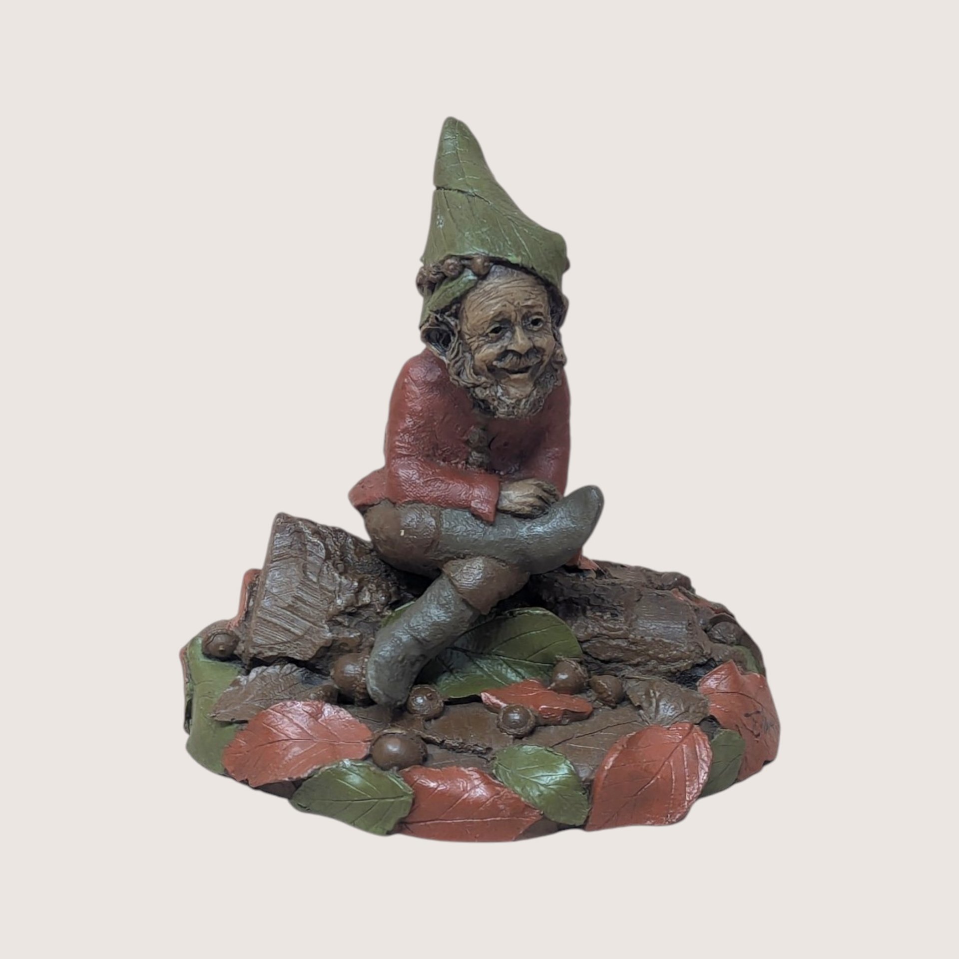 1995 Tom Clark signed Padre gnome figurine sitting on a log base surrounded by autumn leaves on a linen background