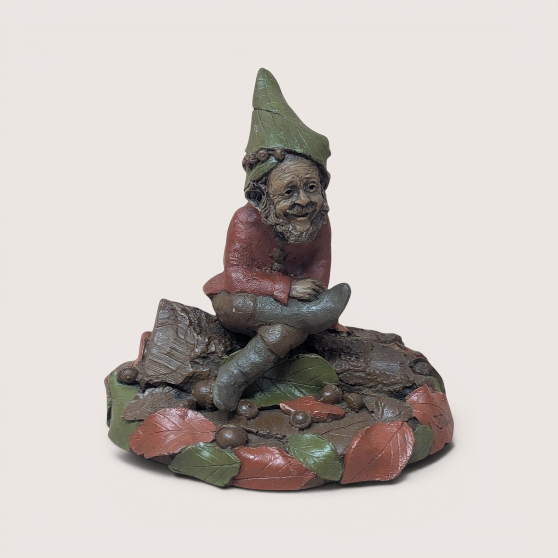 1995 Tom Clark signed Padre gnome figurine sitting on a log base surrounded by autumn leaves on a linen background