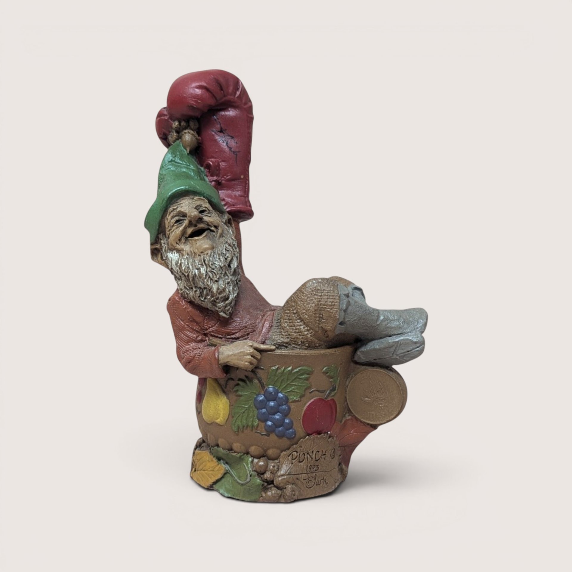 1993 Tom Clark signed Punch gnome figurine inside a fruit bowl wearing a large red boxing glove on a linen background