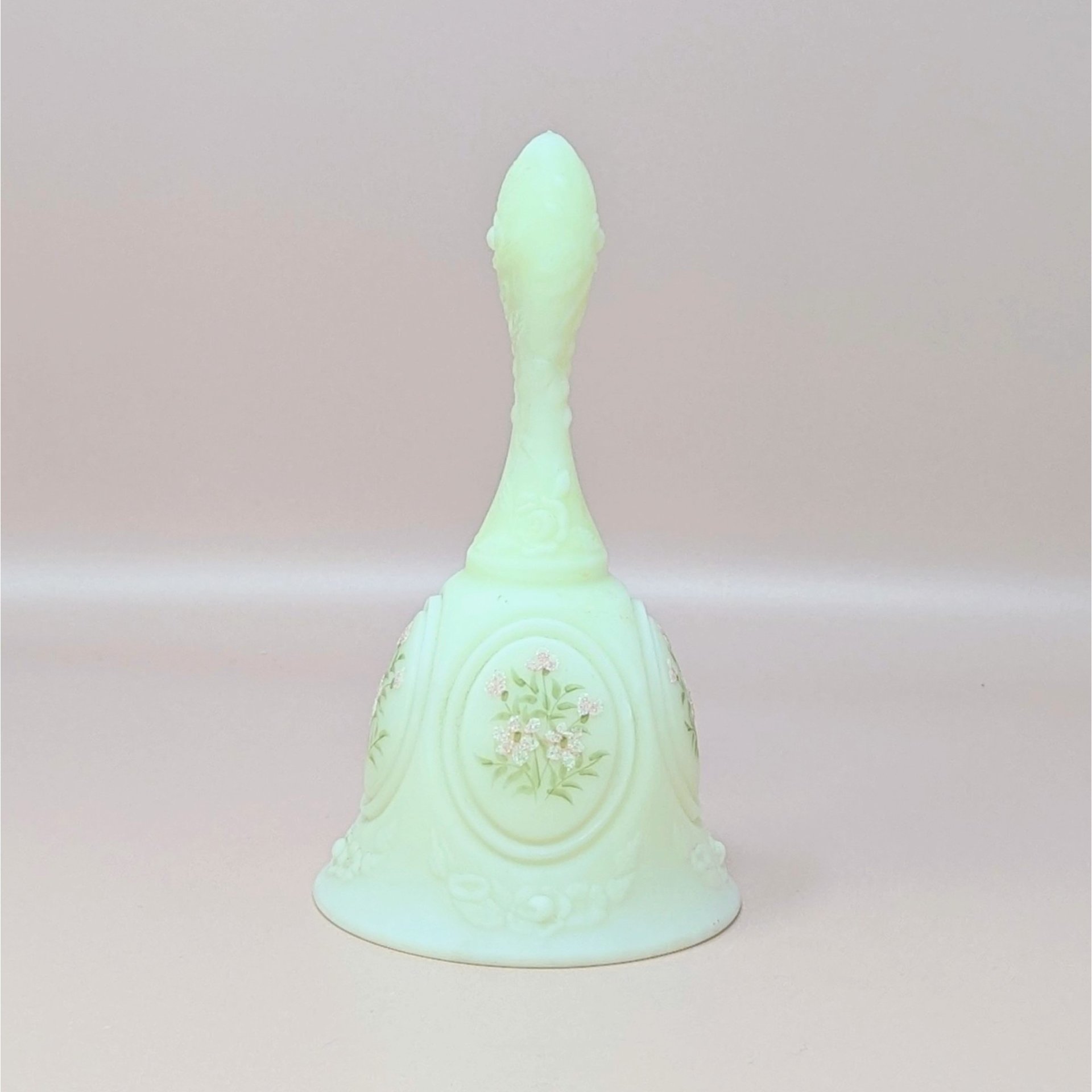 A vintage Fenton custard satin glass bell featuring a hand-painted pink floral spray, signed by artist S. Johnson, set against a neutral background.