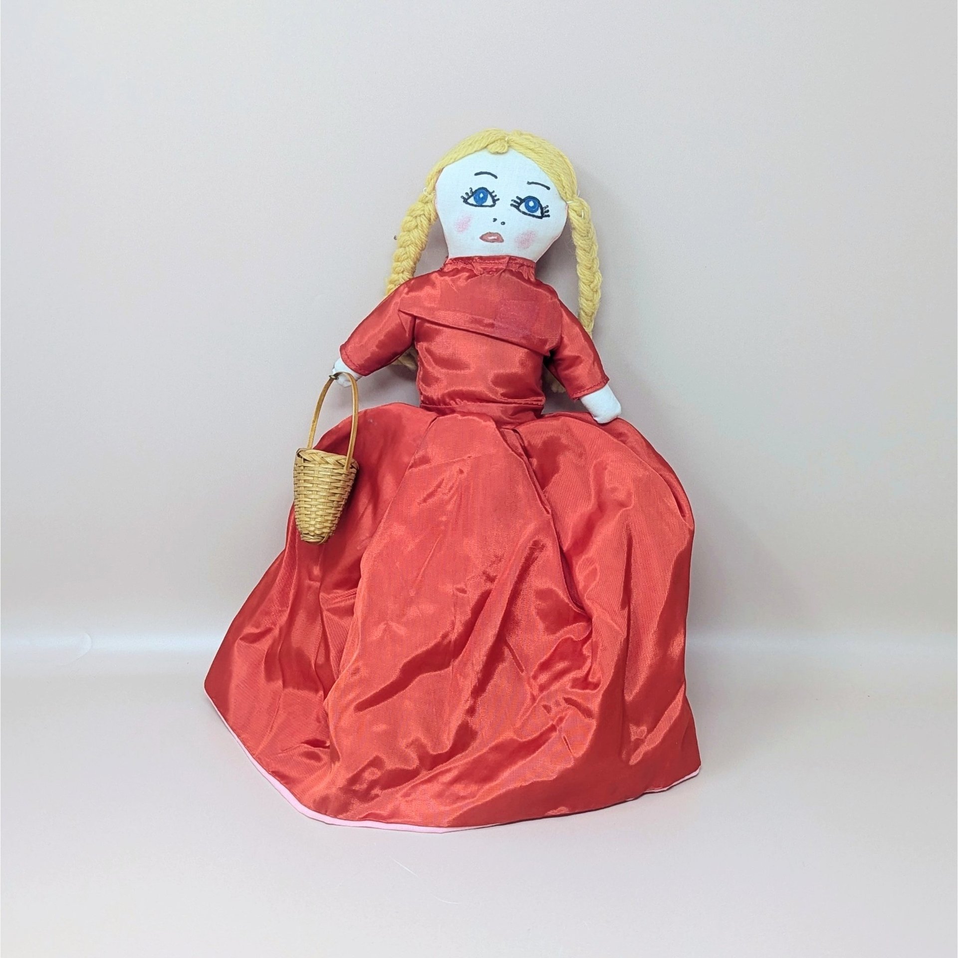 A vintage handmade Topsy Turvy doll with blonde braids and a red dress, featuring a reversible design that reveals a second character, including a small wicker basket pinned to the hand.