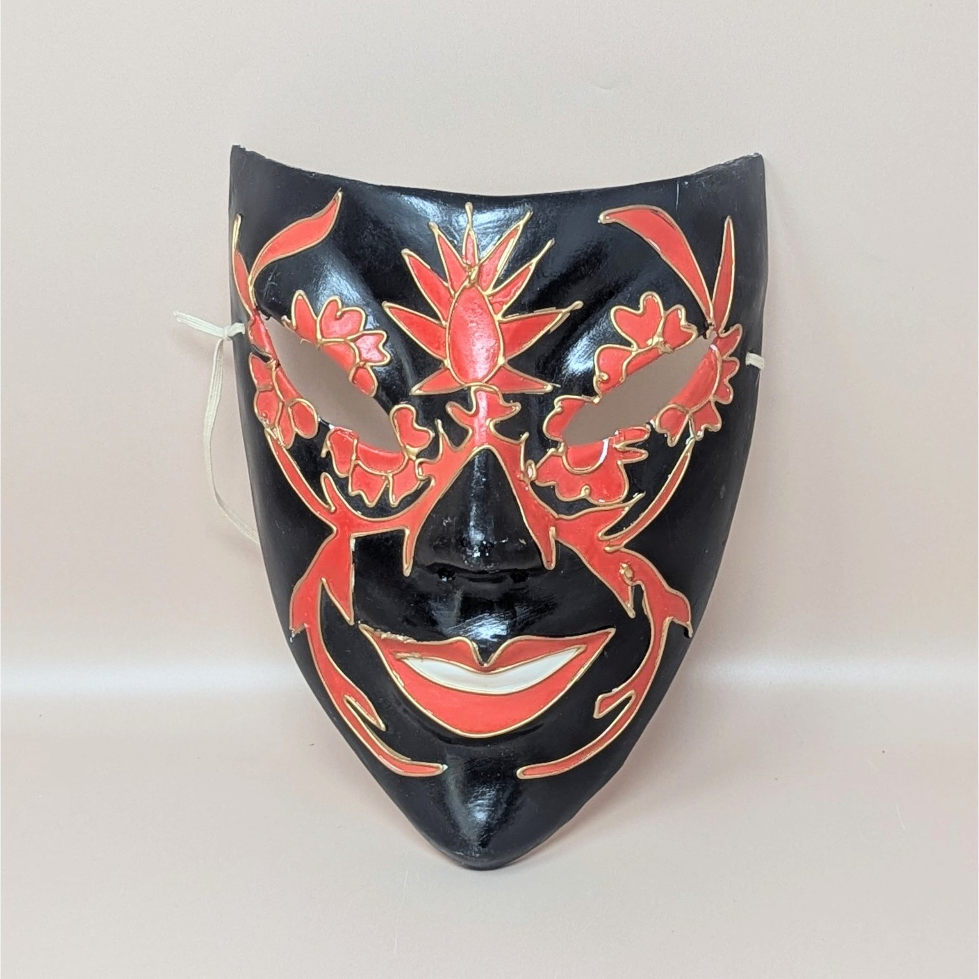 A vintage handmade paper mache wall mask featuring a black base with hand-painted red floral patterns and gold outlines