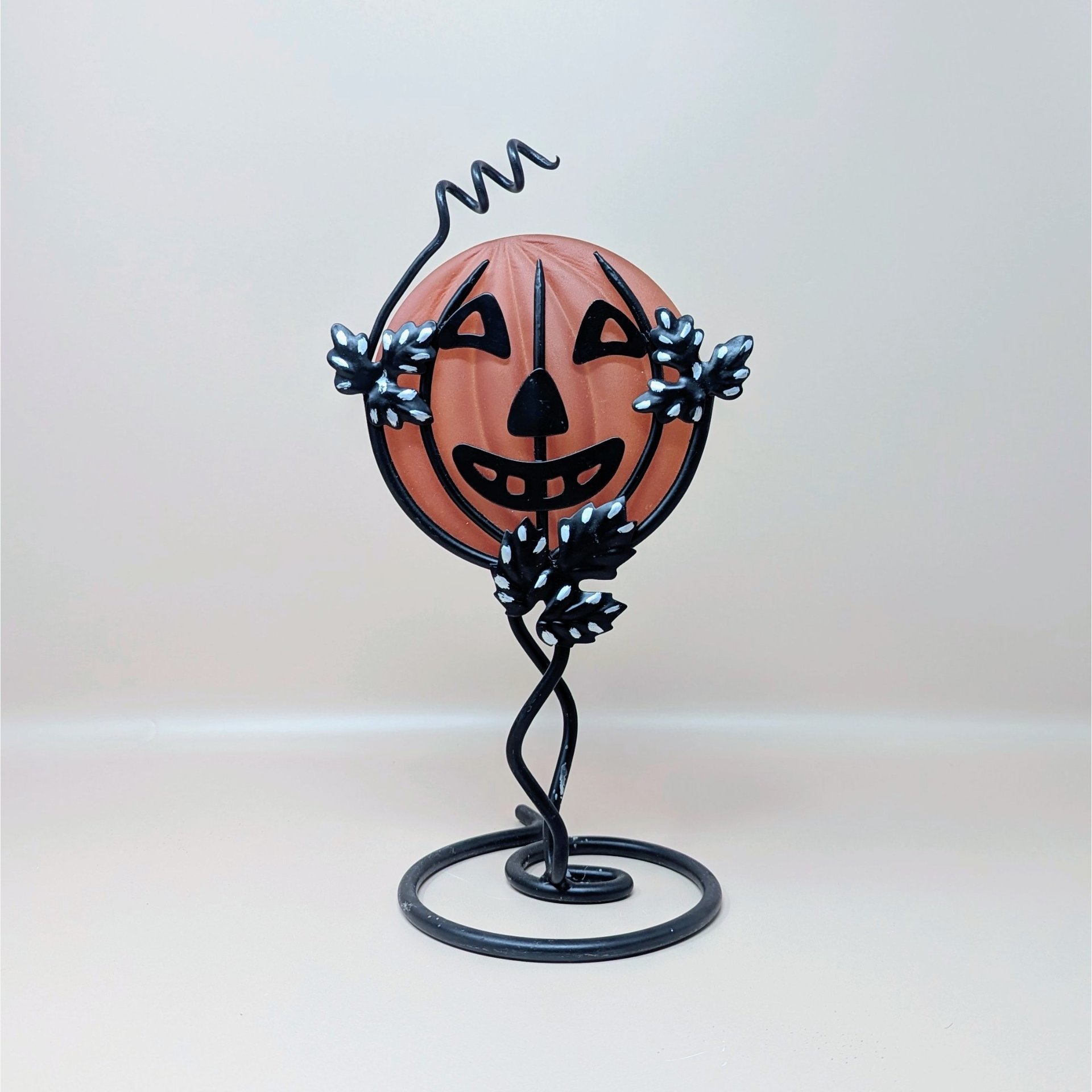 A vintage Department 56 Halloween candle holder featuring a frosted orange glass jack o lantern held within a black metal vine and leaf stand