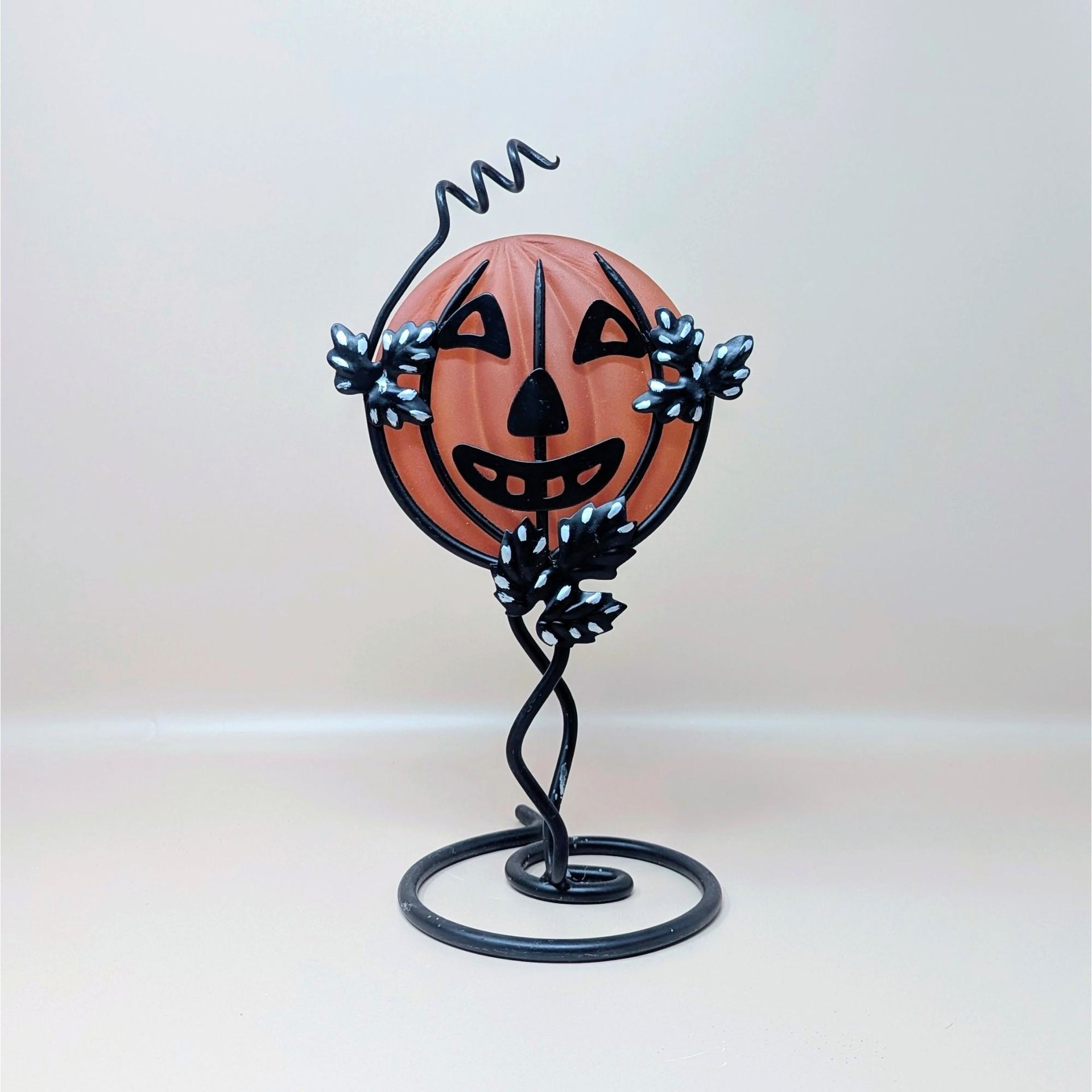 A vintage Department 56 Halloween candle holder featuring a frosted orange glass jack o lantern held within a black metal vine and leaf stand