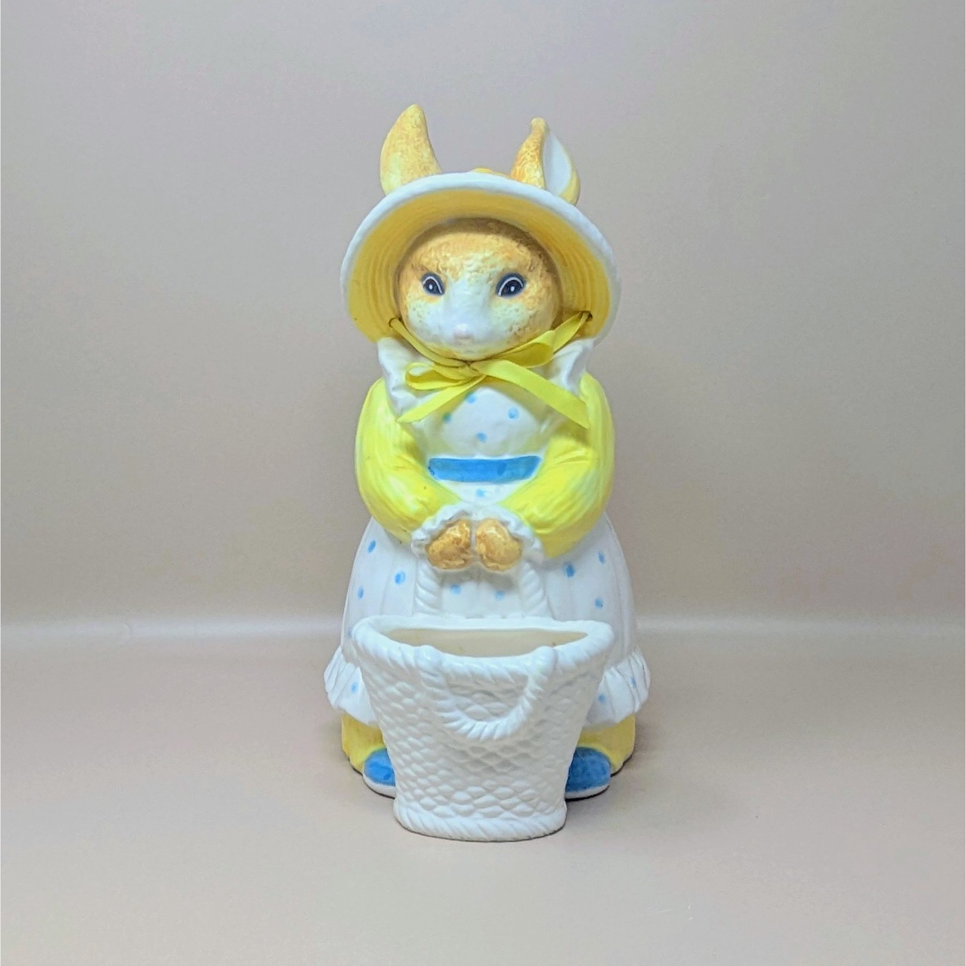 A vintage Department 56 ceramic rabbit planter featuring a mother bunny in a yellow sun hat and blue polka dot apron holding a white basket