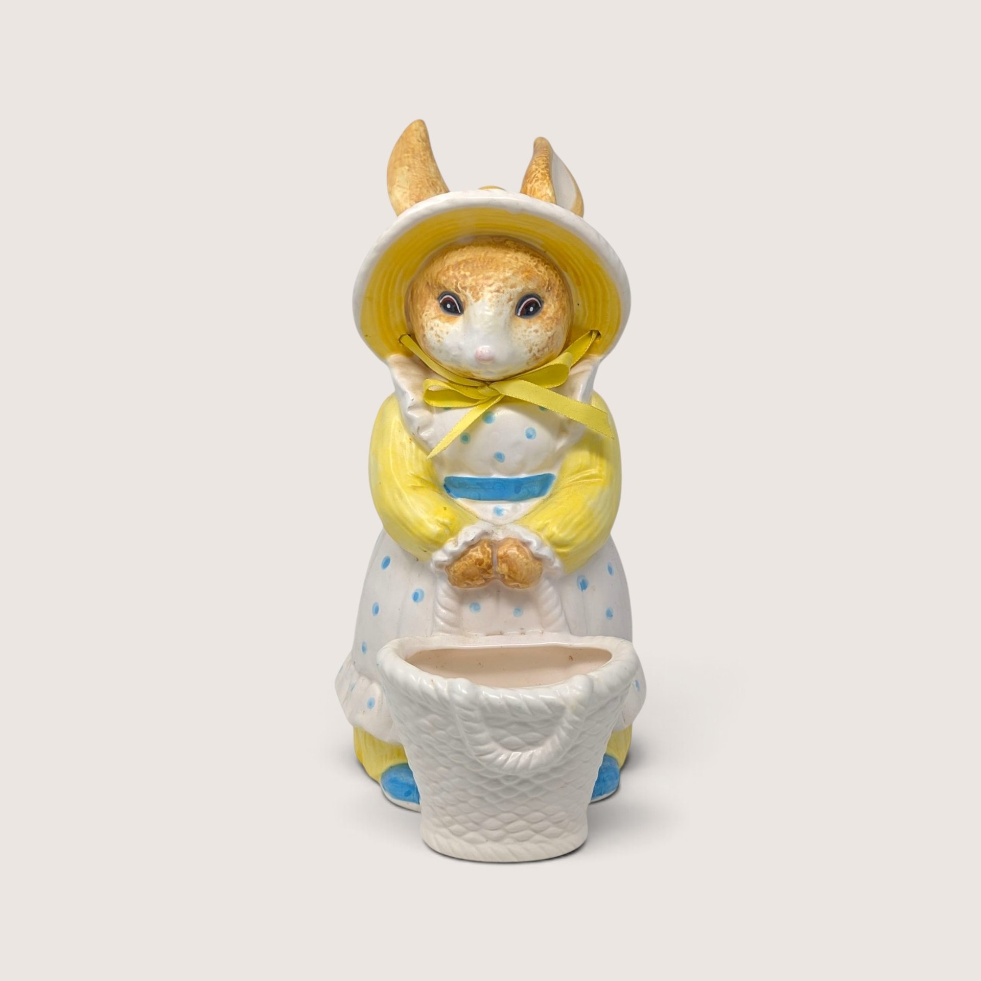Vintage Dept 56 ceramic rabbit planter figurine wearing a yellow bonnet and holding a white basket.
