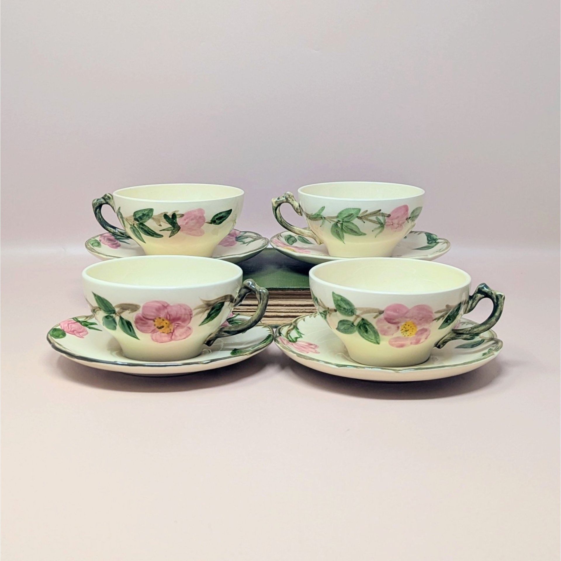 A vintage set of four Franciscan Desert Rose tea cups and saucers featuring hand-painted pink wild roses and green leaves on a cream ceramic base.