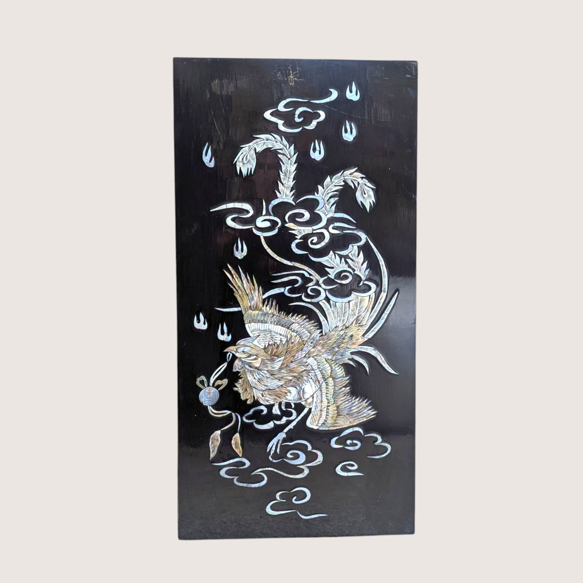 Vintage Asian black lacquer wood wall panel with iridescent mother of pearl inlay depicting a phoenix among clouds on a linen background