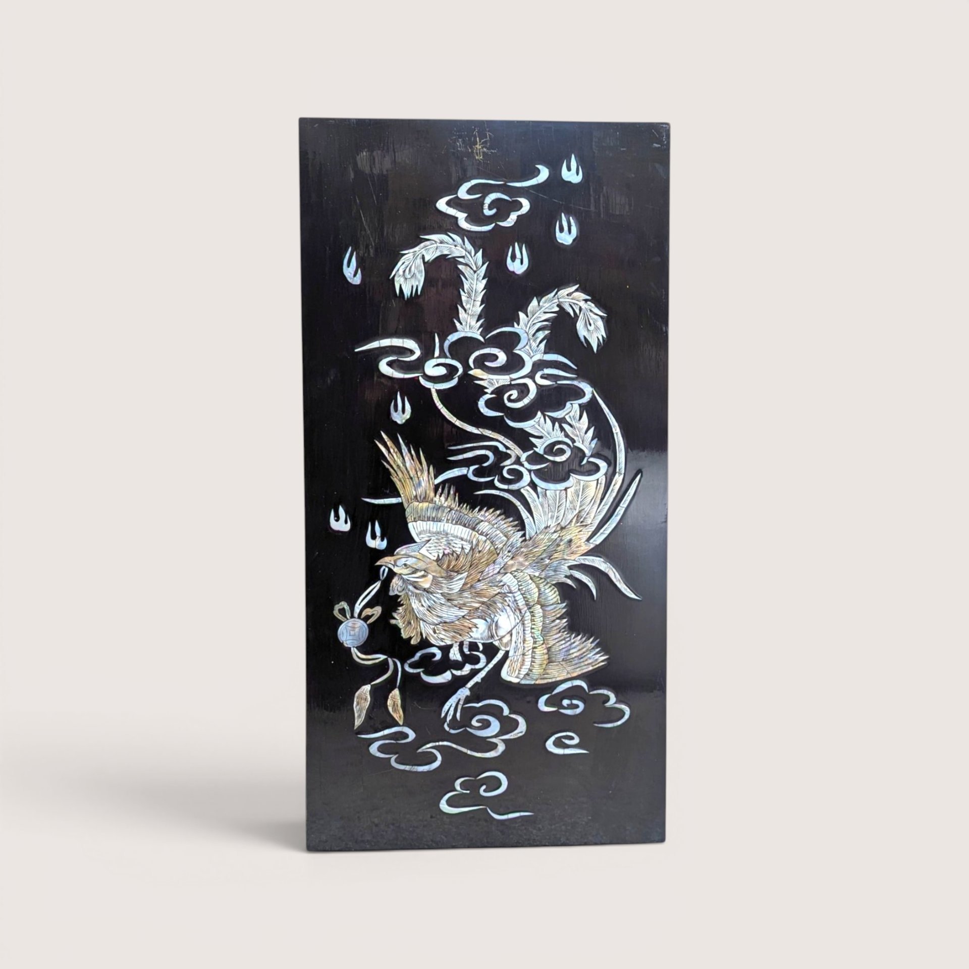 Vintage Asian black lacquer wood wall panel with iridescent mother of pearl inlay depicting a phoenix among clouds on a linen background