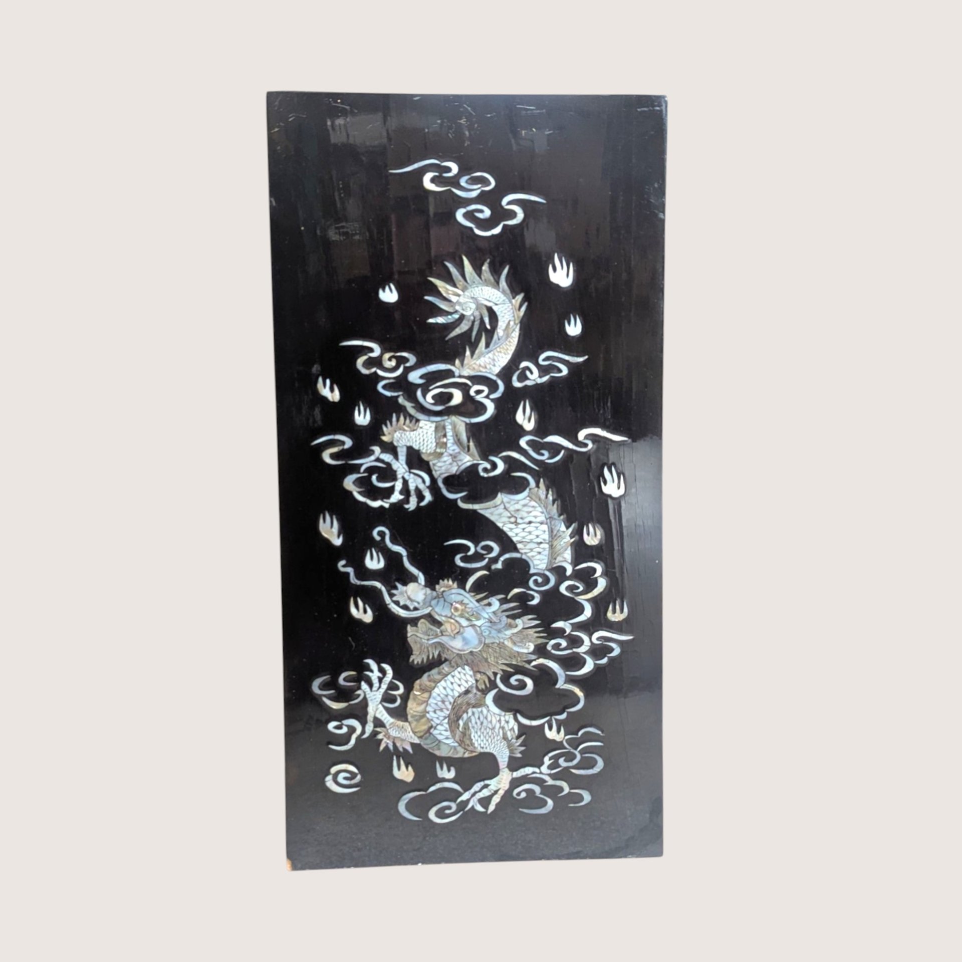 Vintage Asian black lacquer wood wall panel with iridescent mother of pearl inlay depicting a dragon among clouds on a linen background