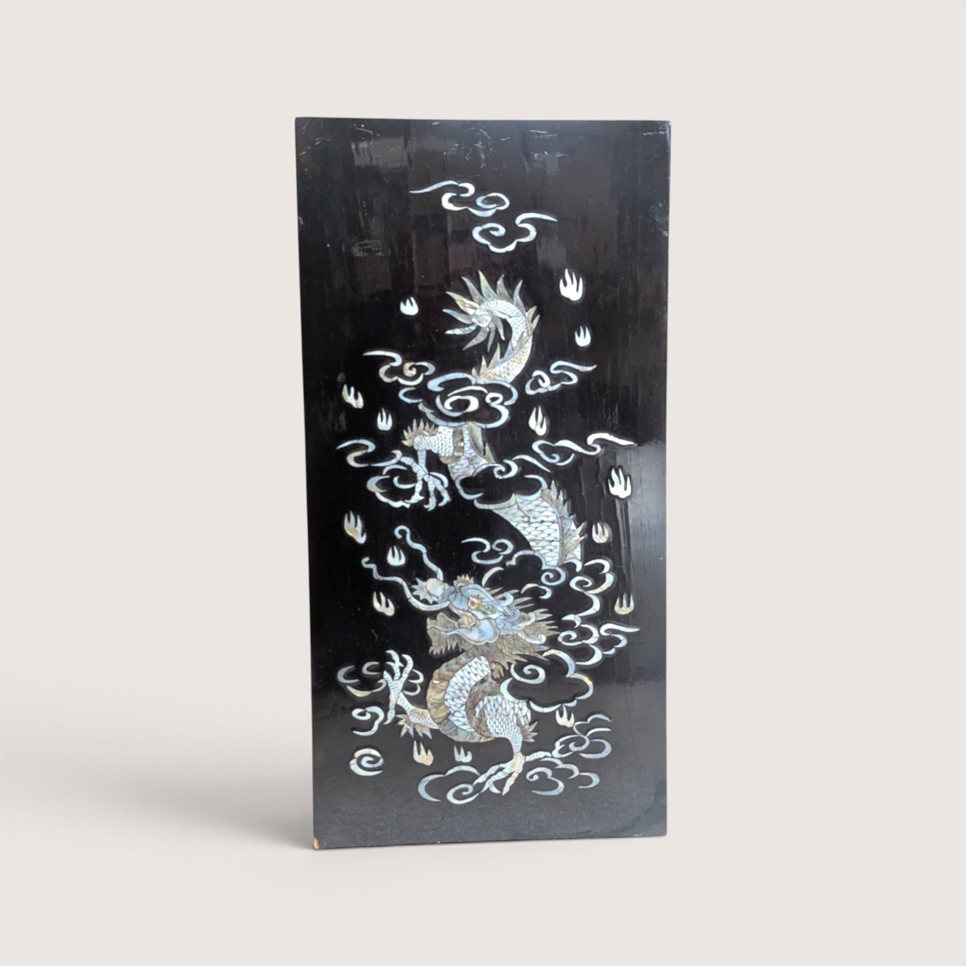 Vintage Asian black lacquer wood wall panel with iridescent mother of pearl inlay depicting a dragon among clouds on a linen background