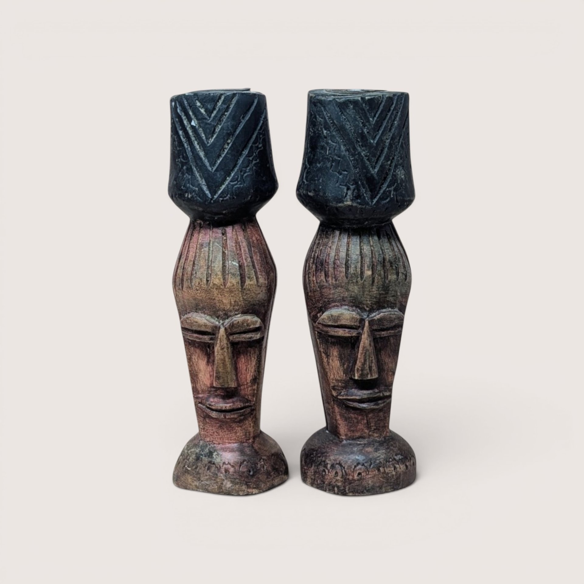 Pair of vintage hand-carved dark wood candlestick holders shaped like stylized African faces with geometric chevron cups.