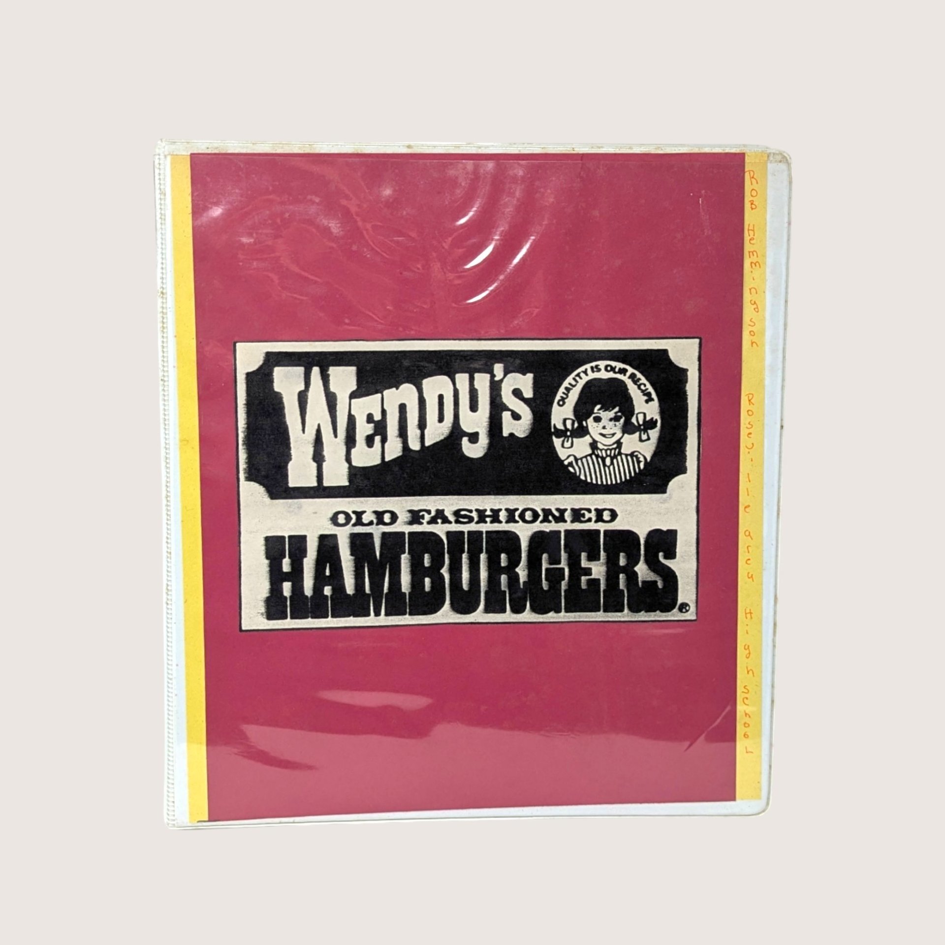 A vintage 1980s Wendy's employee instruction manual in a red three ring binder on a linen background