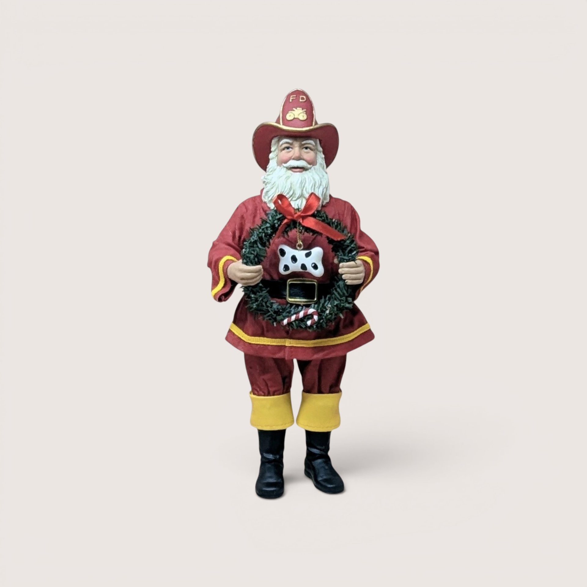 Vintage Fabriche Kurt Adler Santa Claus dressed in a red fireman uniform holding a green wreath with a dog bone.