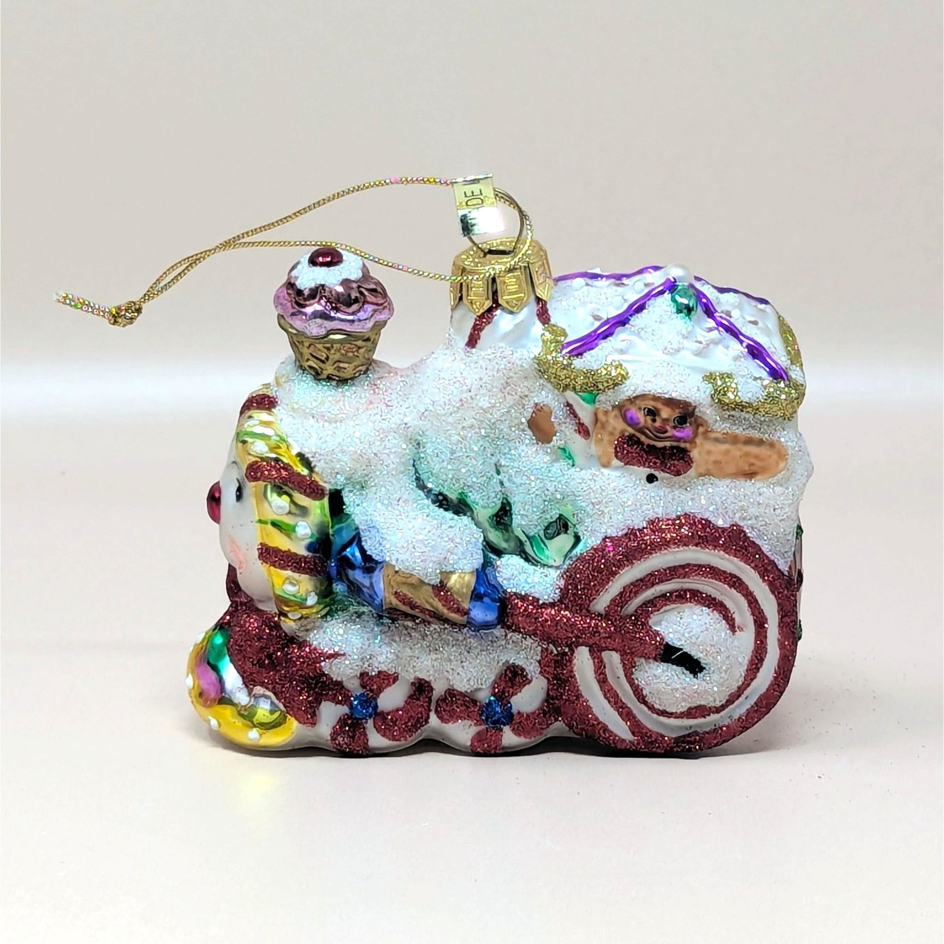 A 2003 Fitz and Floyd blown glass train ornament from the Holiday Treasures collection on a soft pink background. The festive gingerbread style locomotive features vibrant hand painted swirls, a pink cupcake smokestack, and heavy white frosted sugar glitter.