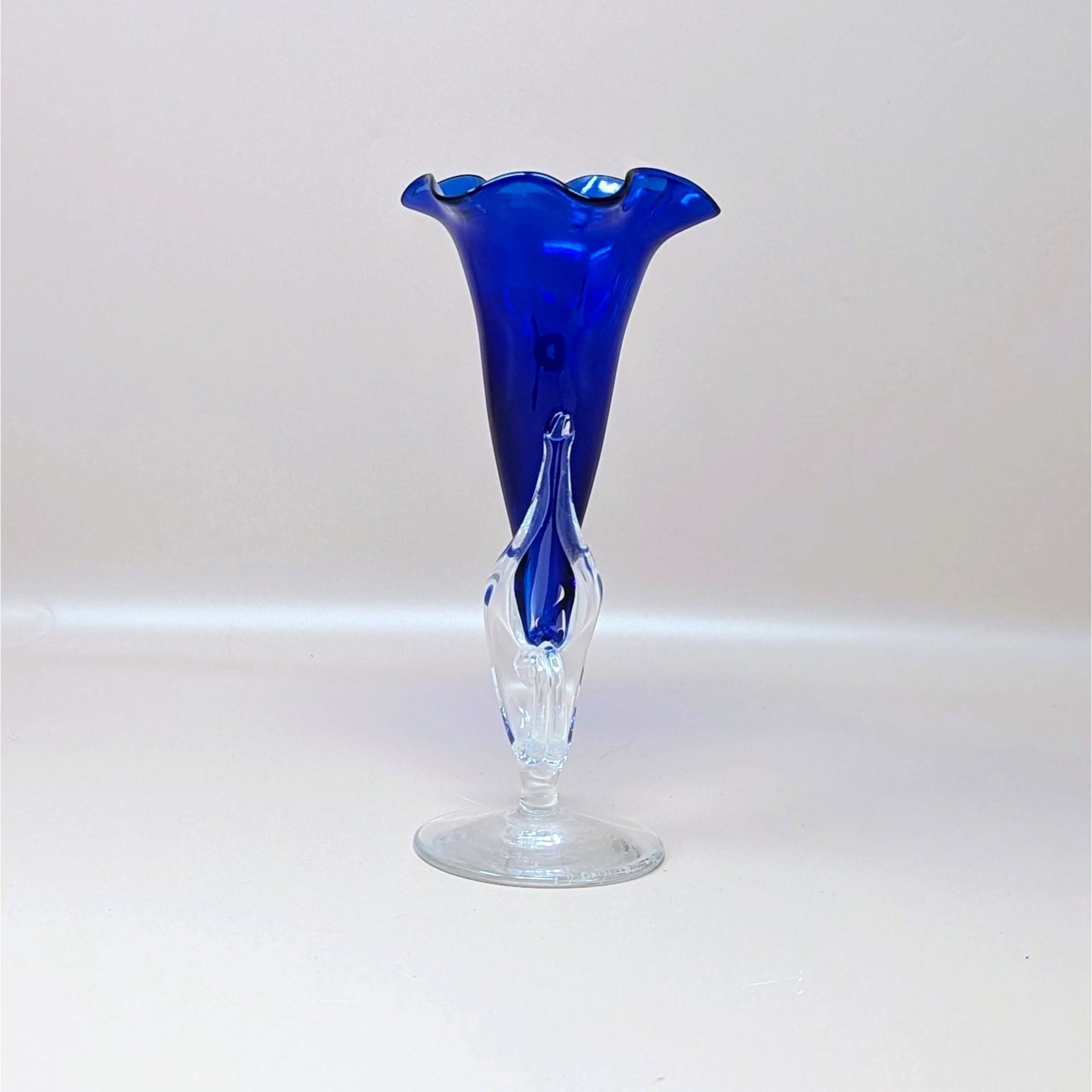A vintage hand blown studio art glass trumpet vase by Dan Dechard on a soft pink background. Made in 1989, the vase features a rich translucent cobalt blue horn set into a clear sculptural stem and circular clear glass base.