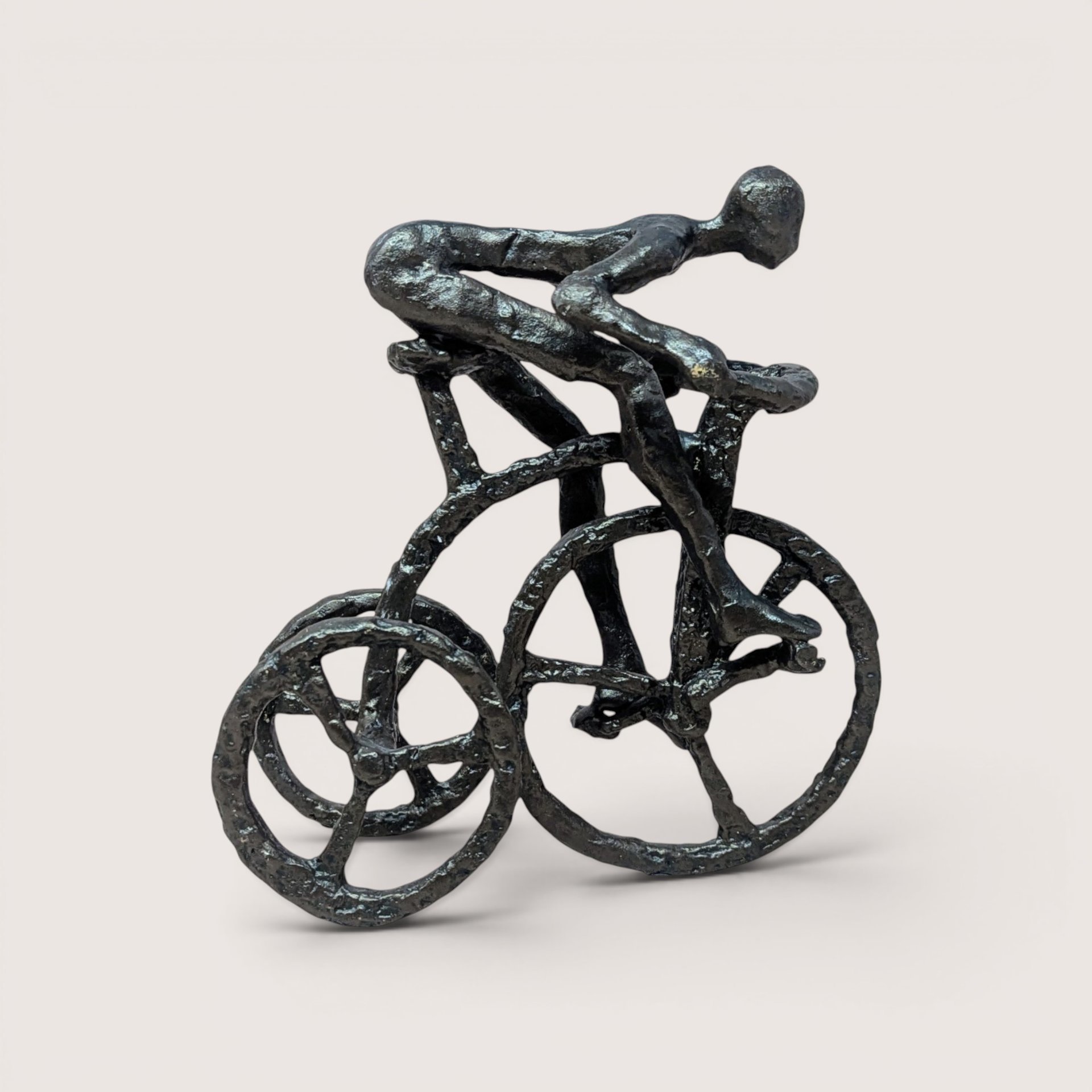 Vintage dark metal brutalist sculpture of a stylized man riding a tricycle on a neutral background.