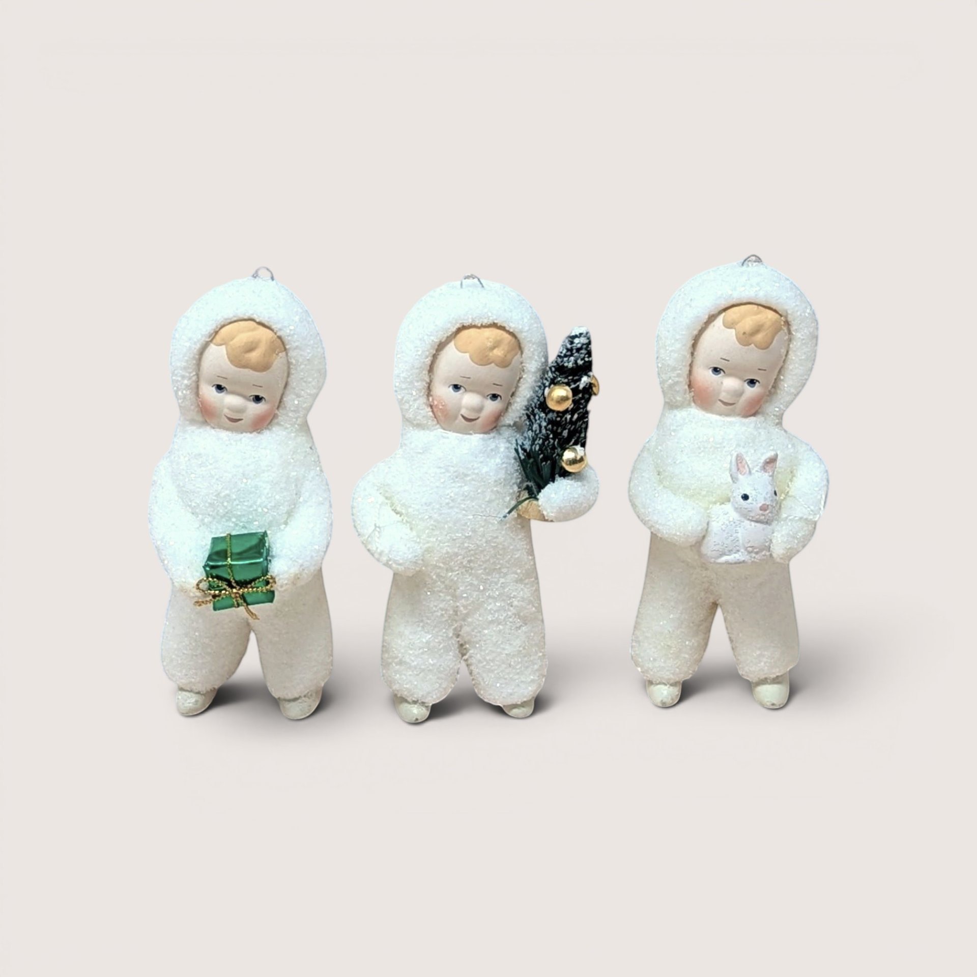 Three Department 56 Snow Angel figurines standing side by side in textured white snowsuits on a plain background
