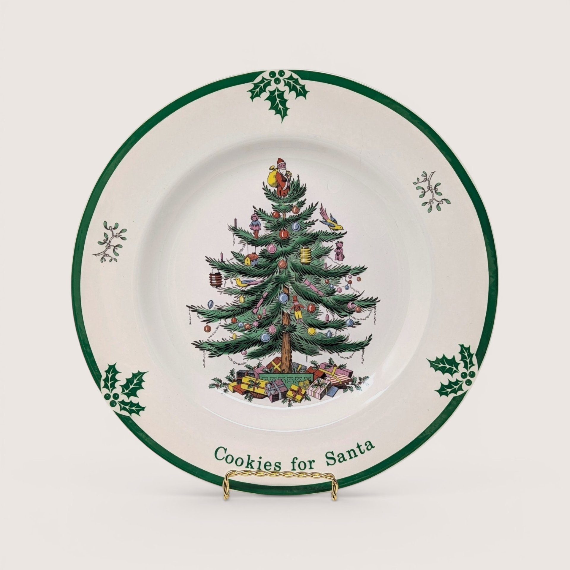 A round cream holiday plate featuring a central decorated Christmas tree design and green border on a plain background