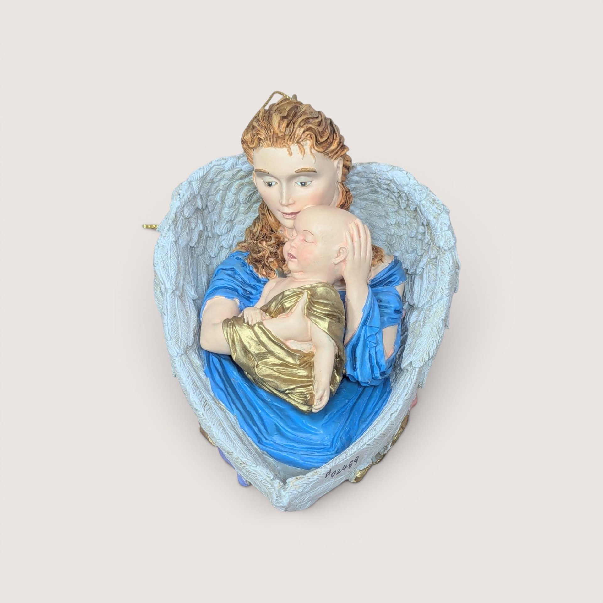 A sculpted resin angel ornament cradling a sleeping baby inside a heart shape formed by her wings on a plain background