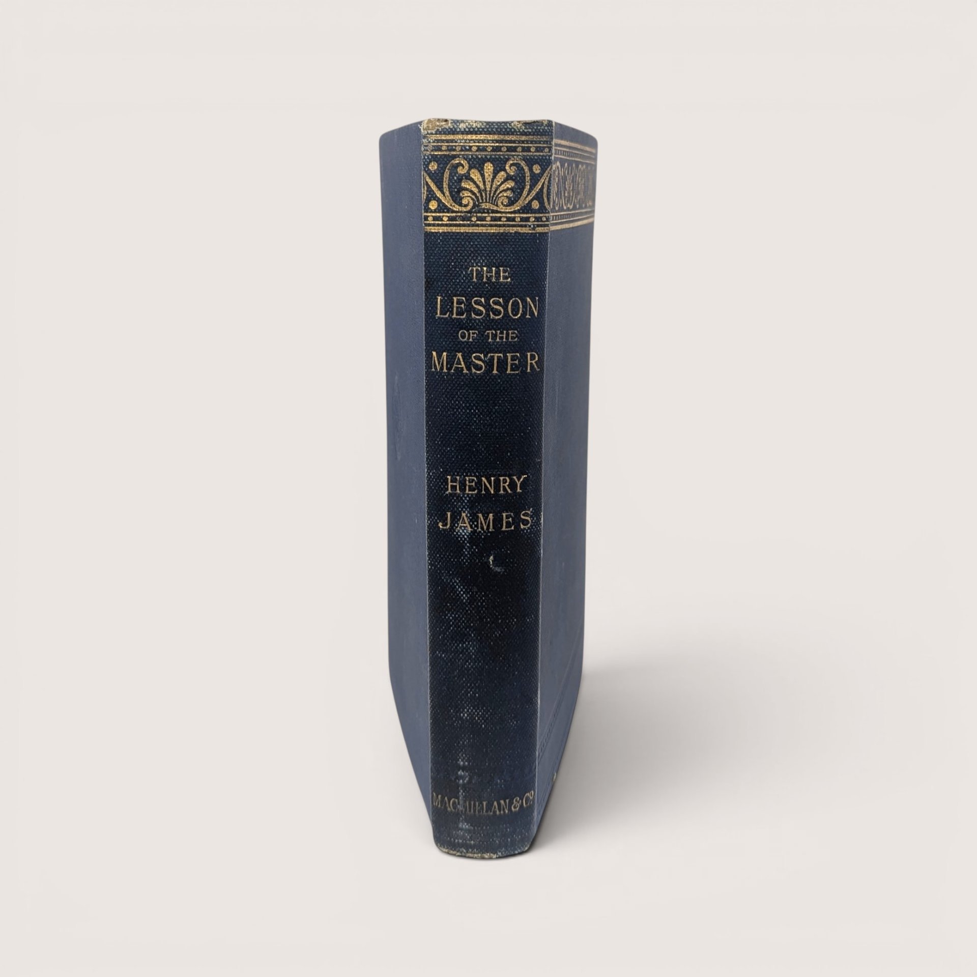 The blue spine of a vintage hardcover book featuring ornate gold gilt decorations and lettering on a plain background