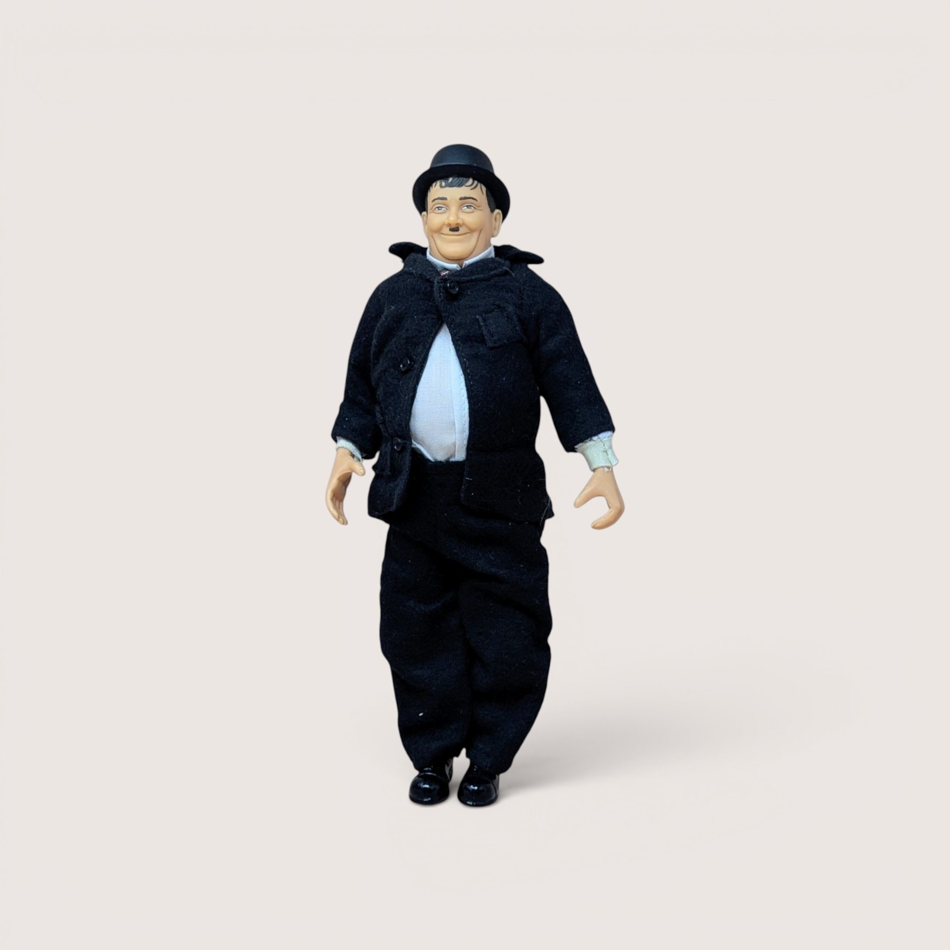 A vintage Oliver Hardy jointed action figure wearing a black suit and bowler hat standing on a plain background