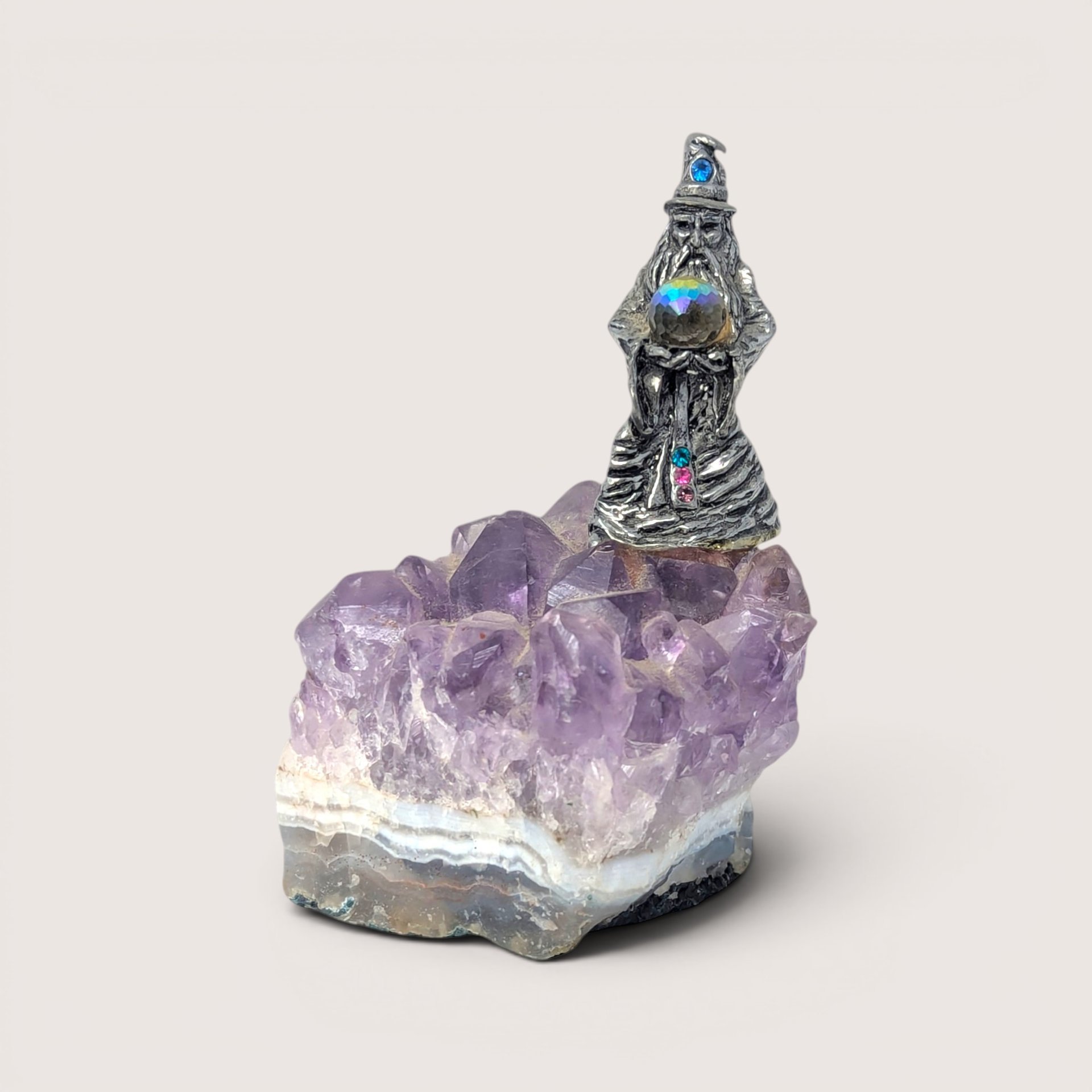 A pewter wizard figurine holding a crystal ball, mounted on a purple amethyst crystal cluster geode base.