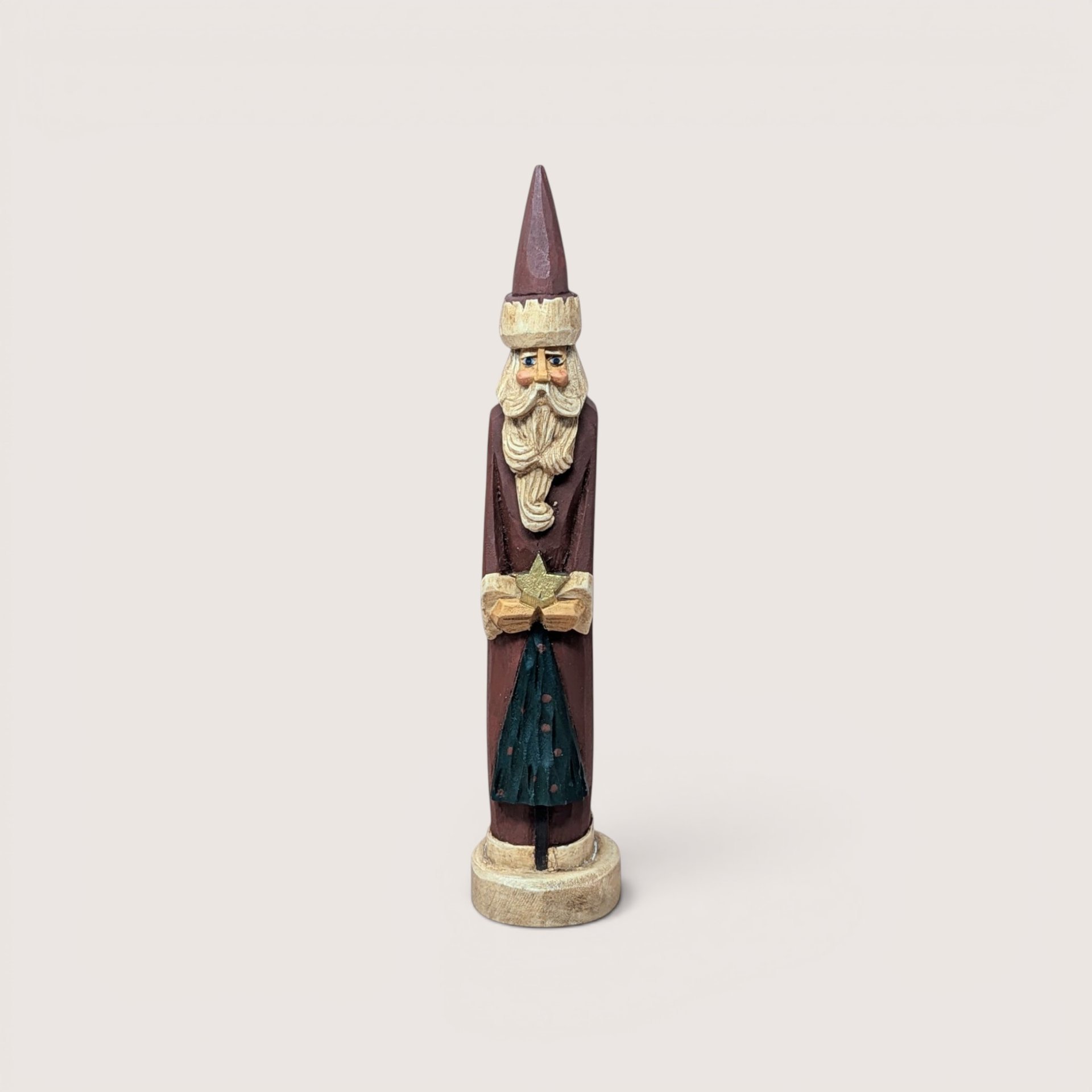 A tall, slender vintage hand-carved wooden Santa Claus figurine holding a gold star above a small green tree.