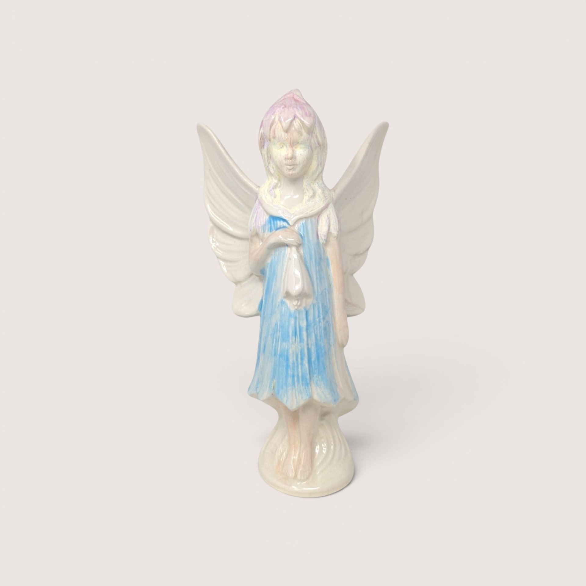 A vintage hand-painted ceramic fairy figurine with large white wings, a blue dress, and iridescent pastel hair.