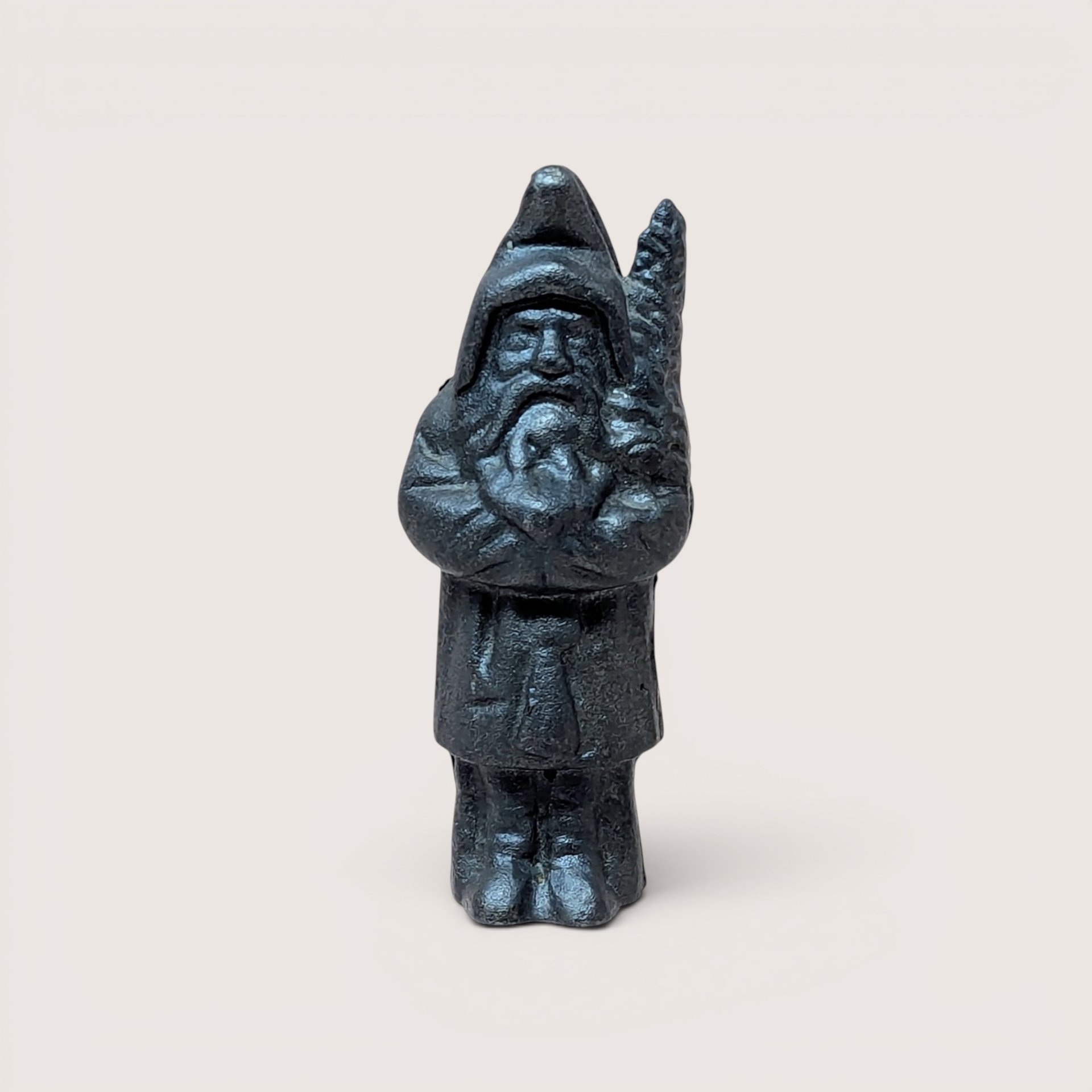 A dark charcoal gray heavy cast iron still coin bank shaped like a whimsical bearded gnome figure holding a tree branch.