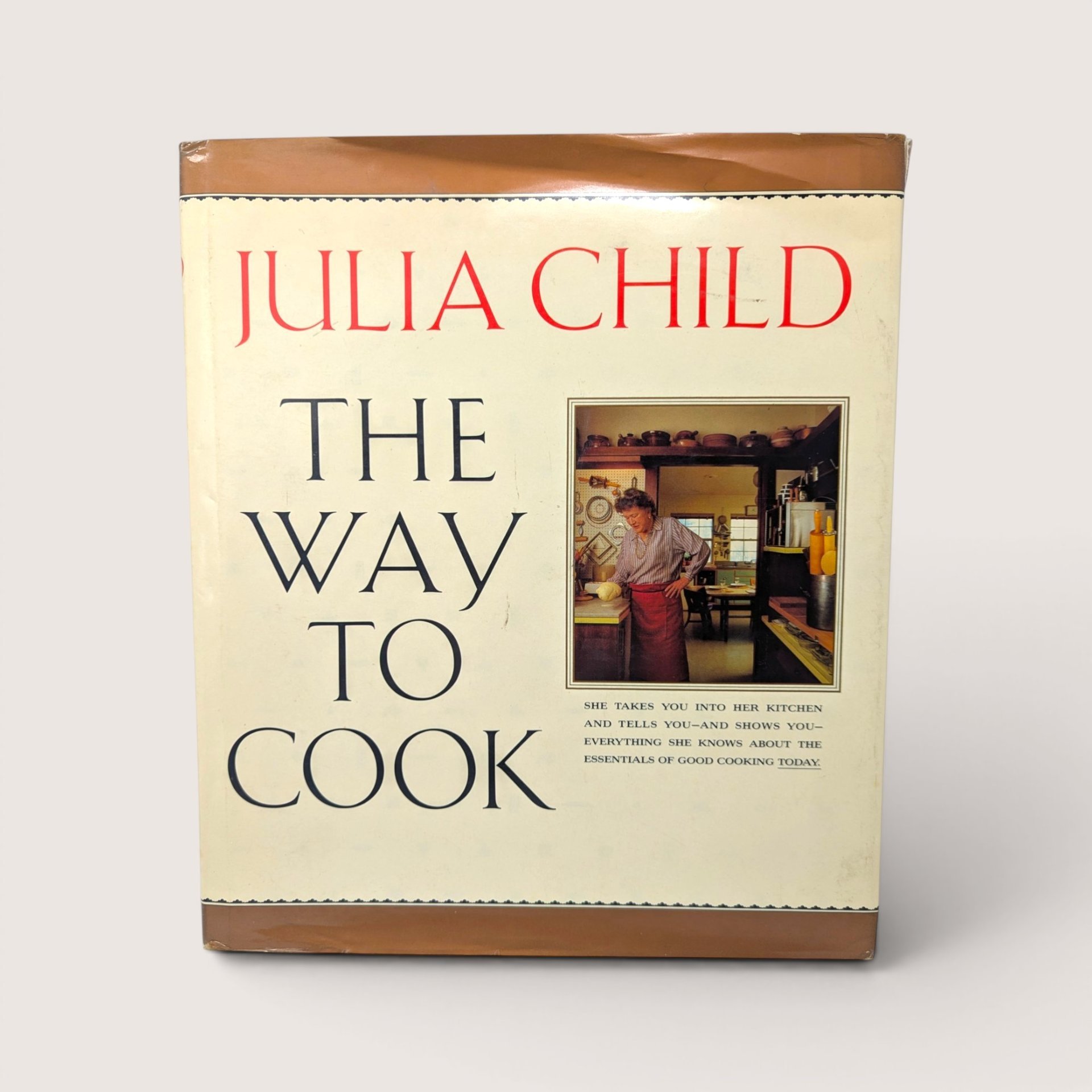 A vintage hardcover copy of The Way To Cook by Julia Child with an image of her in the kitchen on the front dust jacket