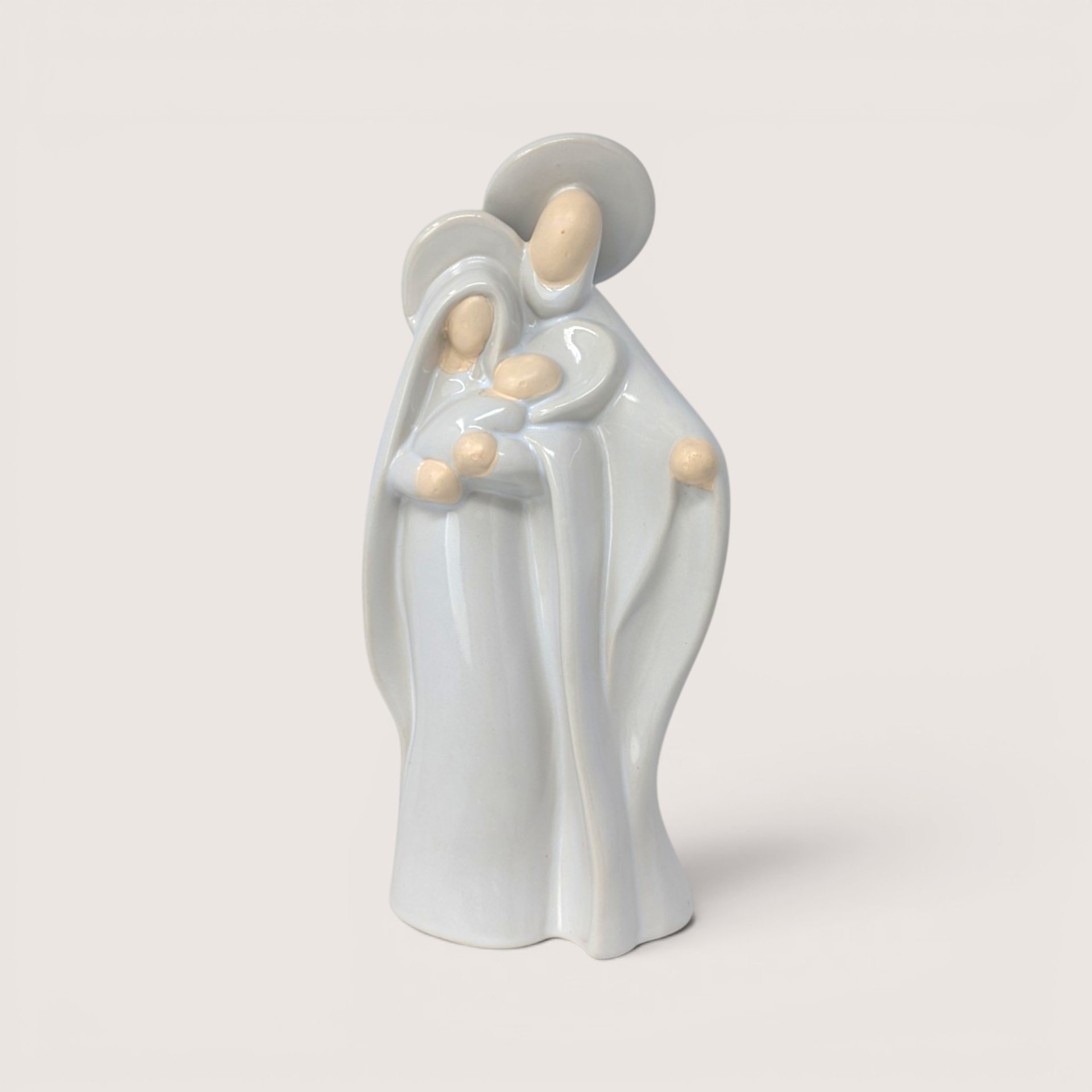 A minimalist light blue and cream ceramic figurine of Mary Joseph and baby Jesus on a solid plain background
