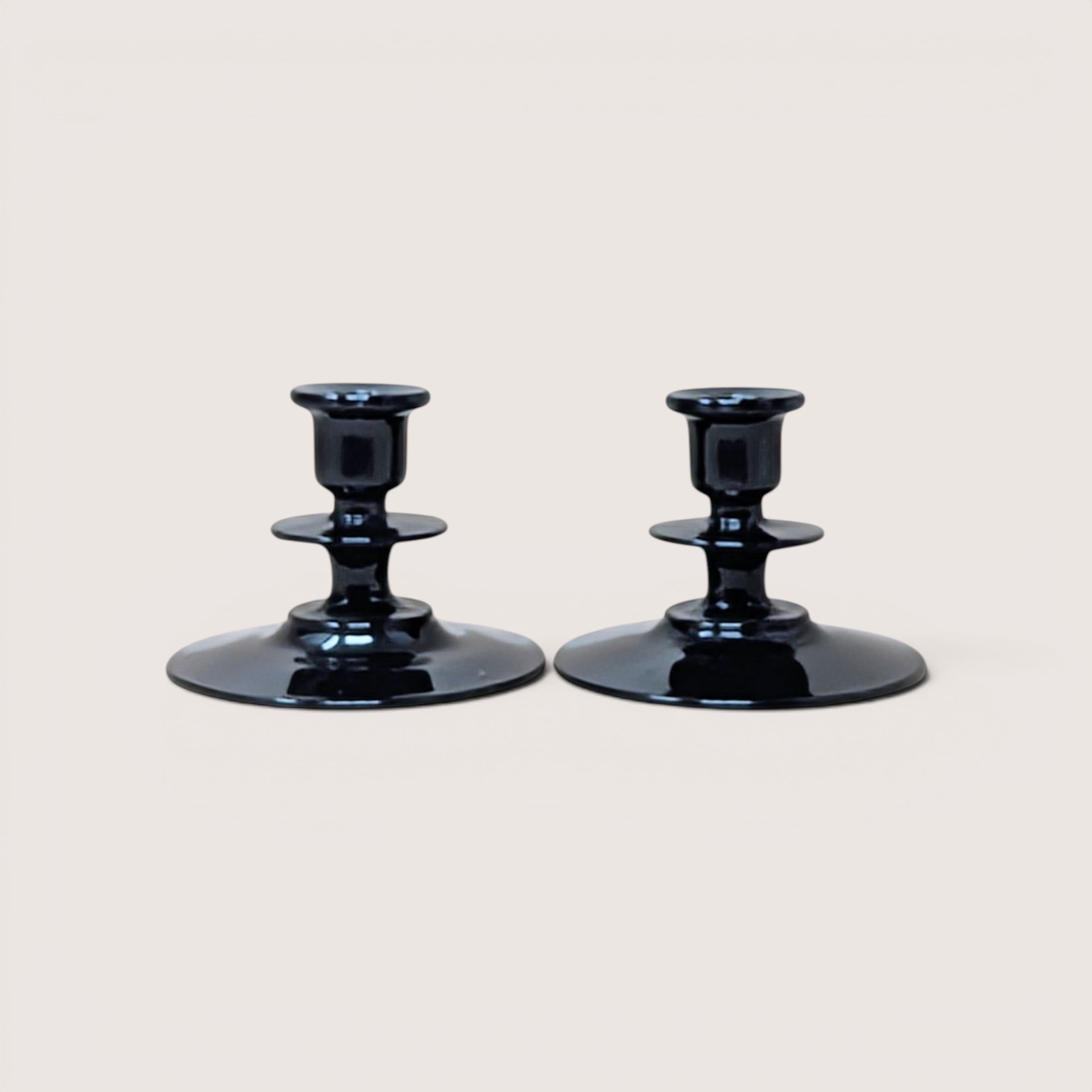 A pair of vintage black glass candle holders with tiered stems and wide round bases on a plain background