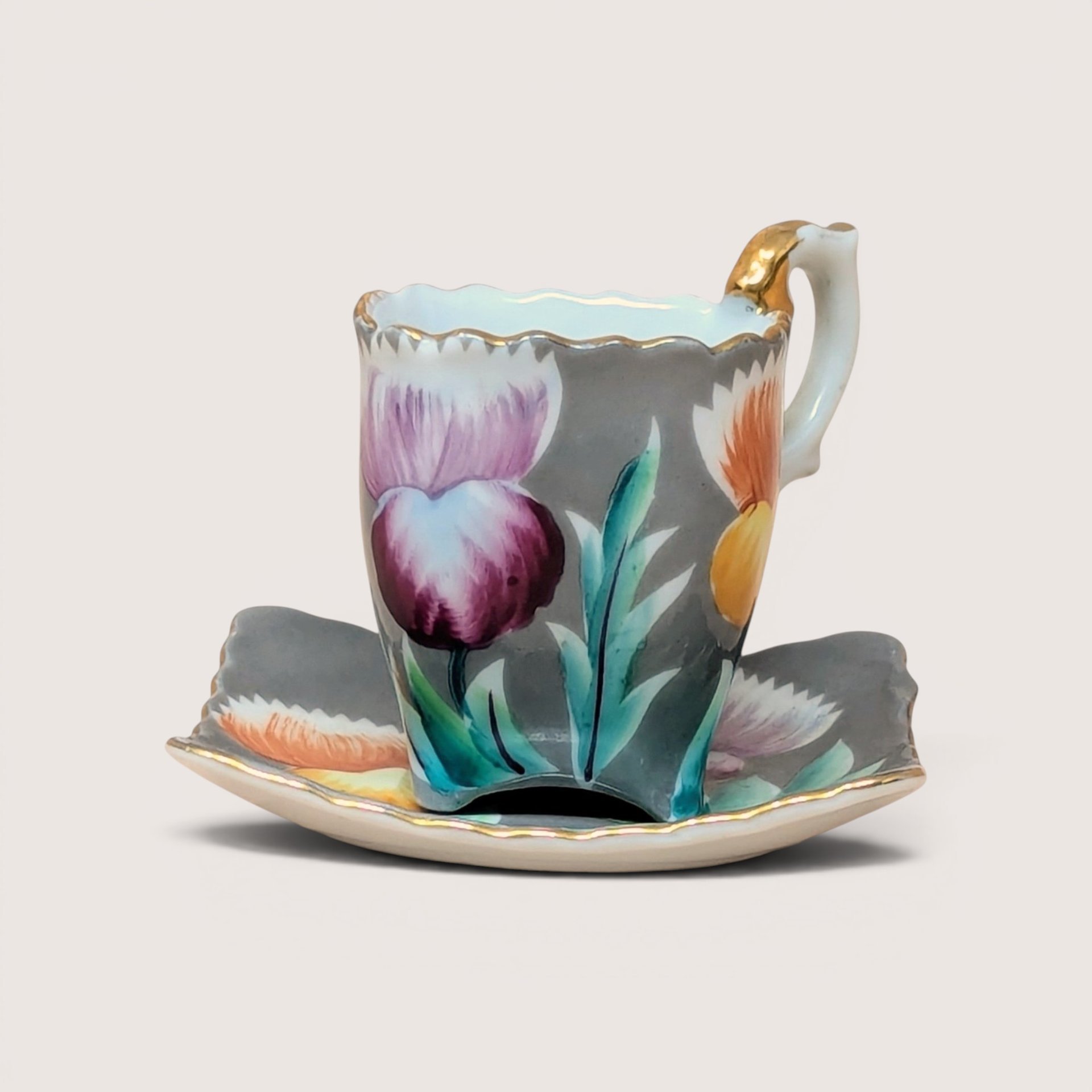 A vintage demitasse cup and saucer with painted purple thistles and gold trim on a plain background