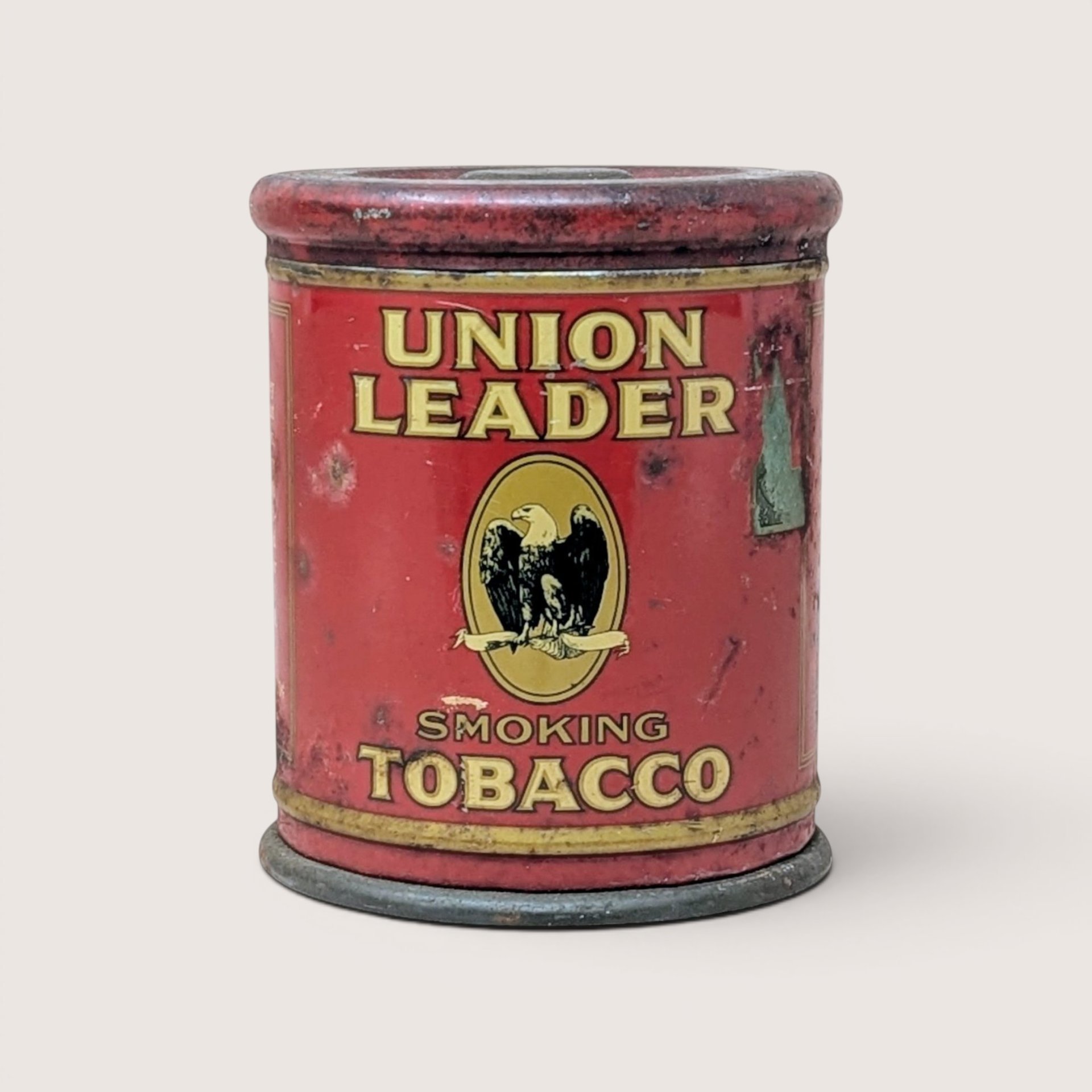 A vintage red Union Leader Smoking Tobacco cylindrical tin with an eagle emblem on a plain background