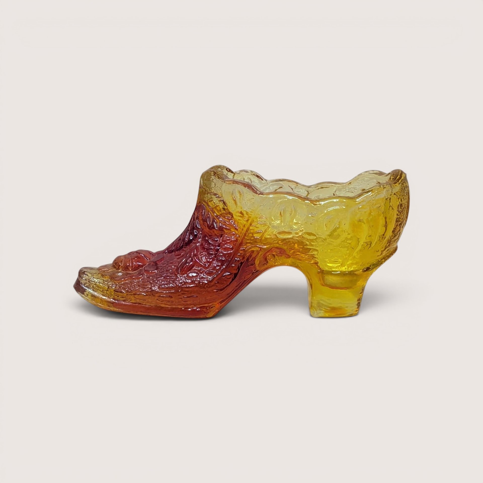 A vintage amberina glass slipper figurine with a textured daisy and button pattern on a plain background