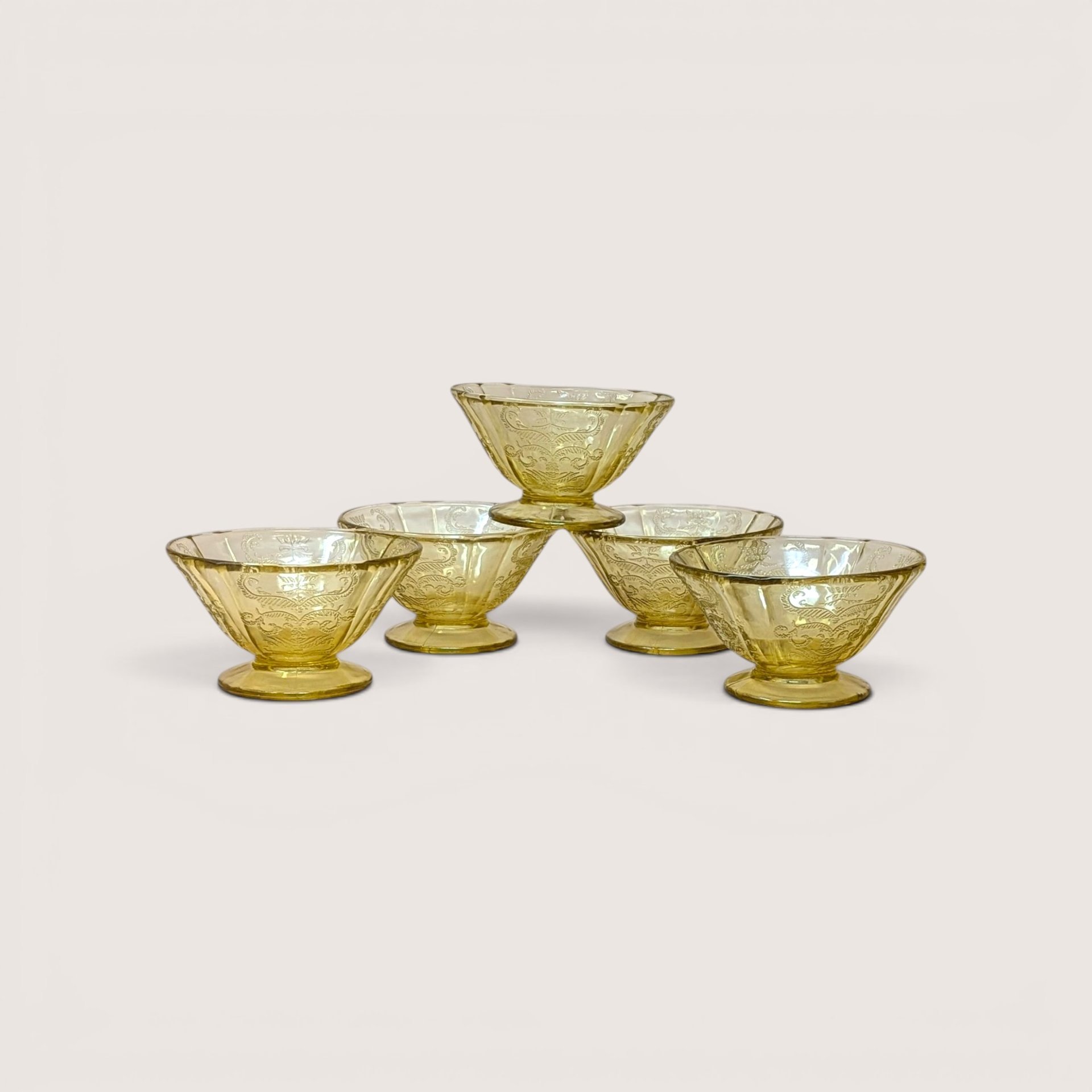 Five amber depression glass sherbet cups stacked in a pyramid on a light beige backdrop