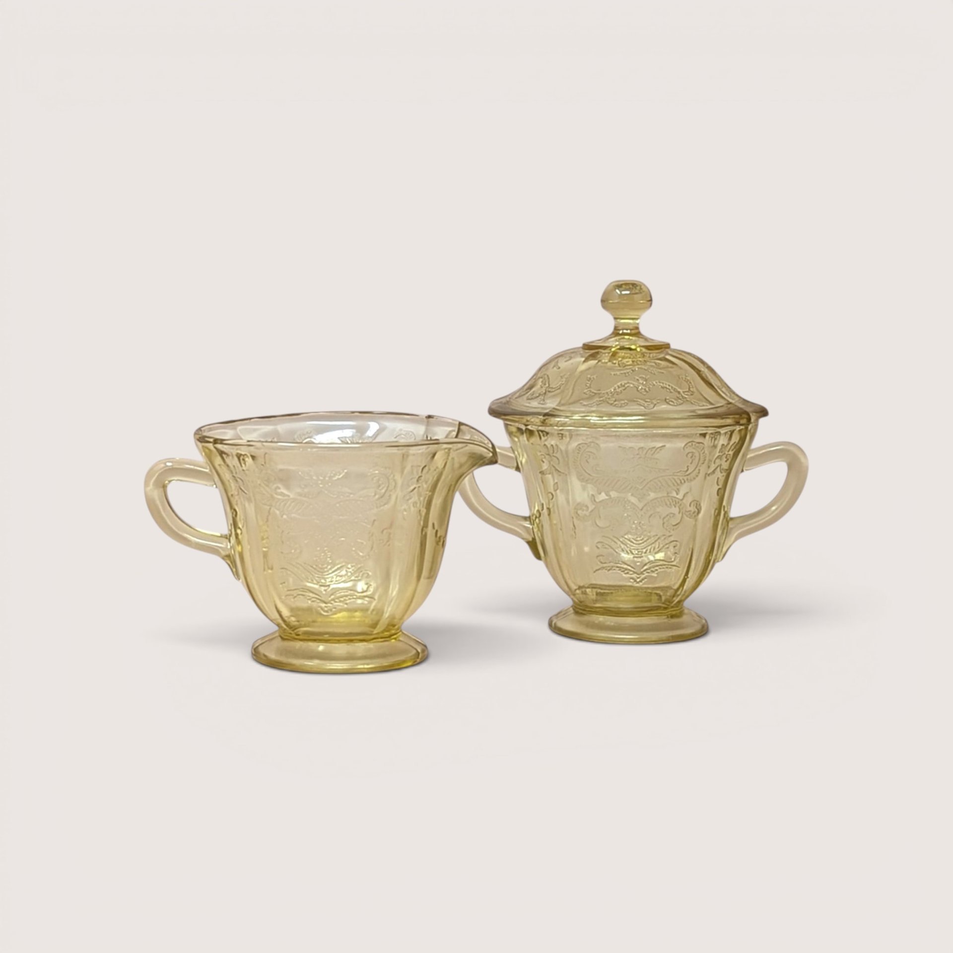 A vintage amber depression glass creamer and matching lidded sugar bowl with a molded scroll pattern on a plain background