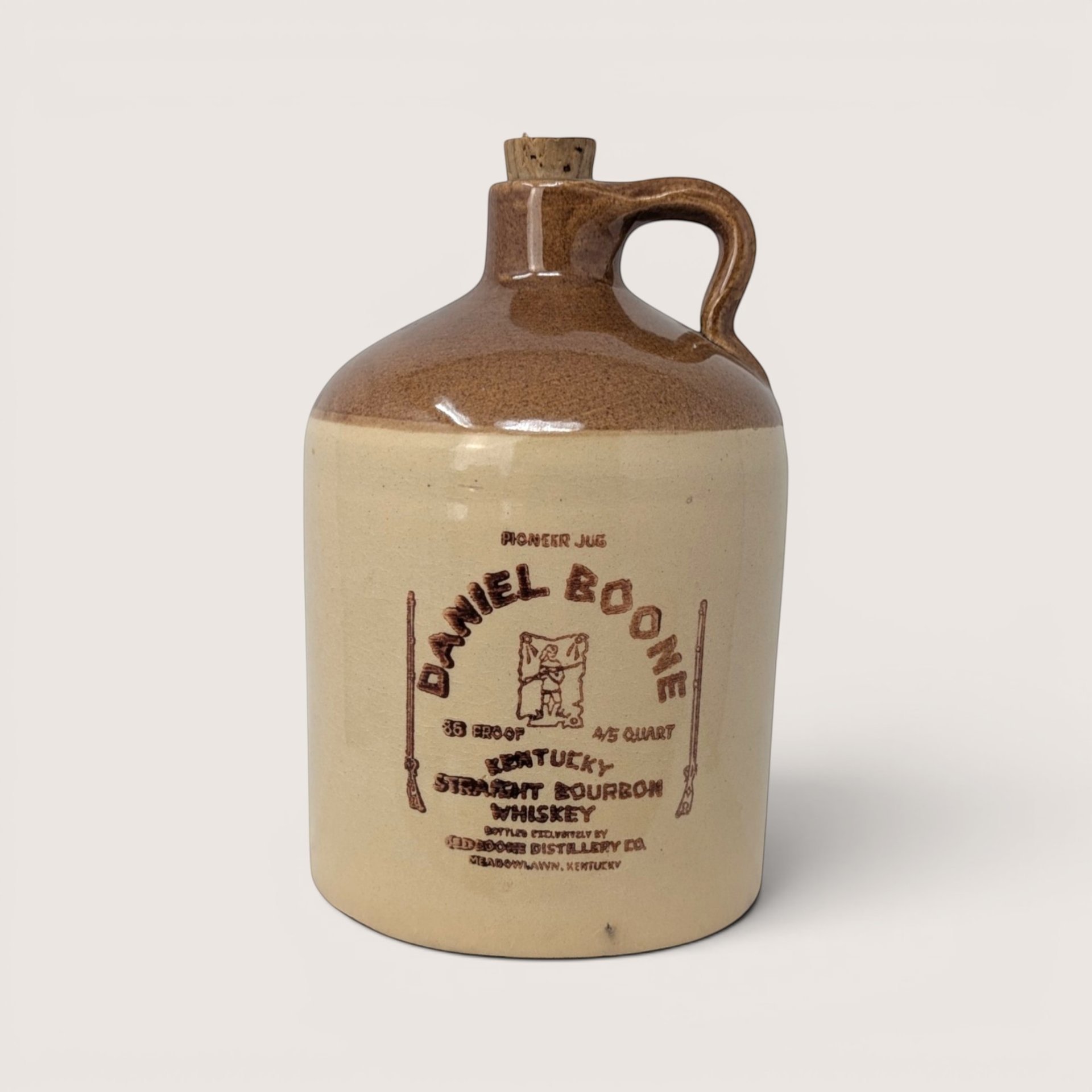 A vintage two tone stoneware Daniel Boone bourbon whiskey jug with a cork stopper on a light cream background